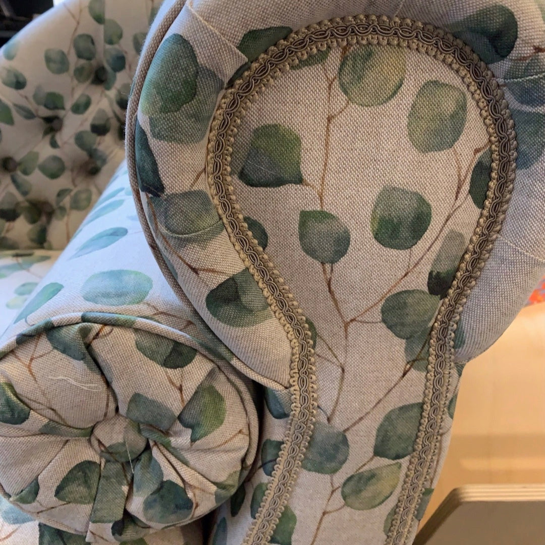 A handcrafted chaise lounge with cream leaves cotton fabric, mahogany stained legs, and brass-colored castors.