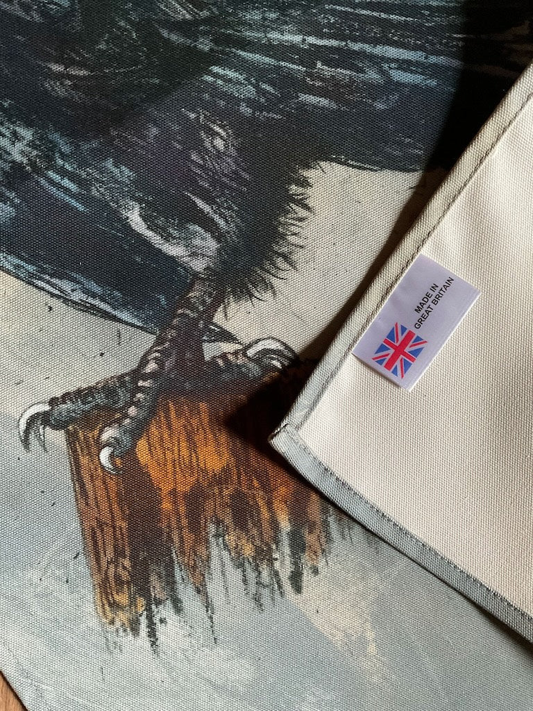 A tea towel featuring an illustration of a standing black crow, against a grey background.