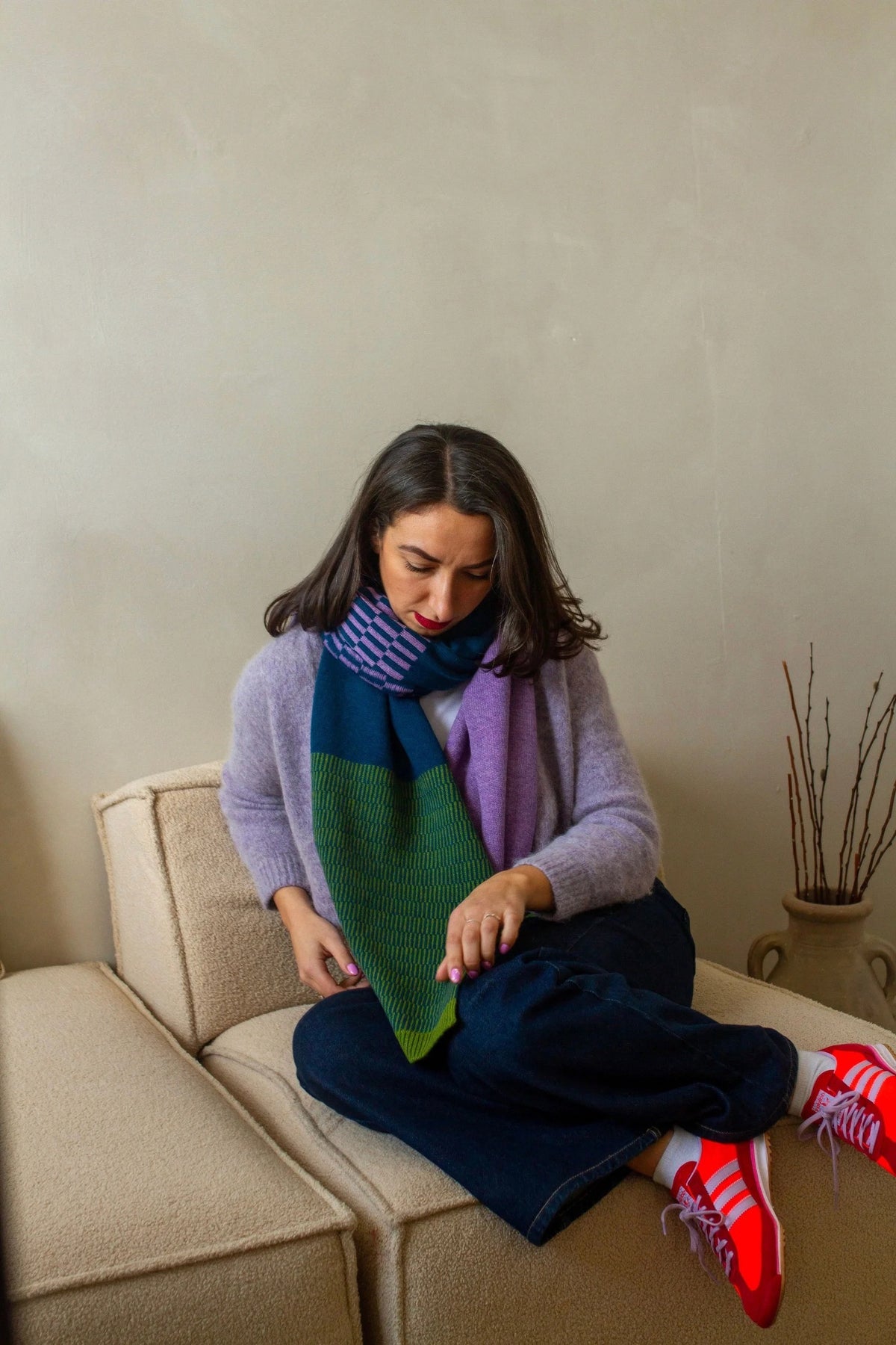 Woman sitting on a couch wearing a colourful knitted scarf and red shoes.