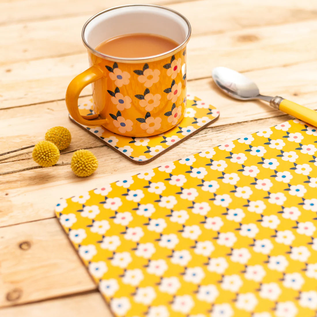 A yellow floral placemat and matching coaster and mug on a light wood table.