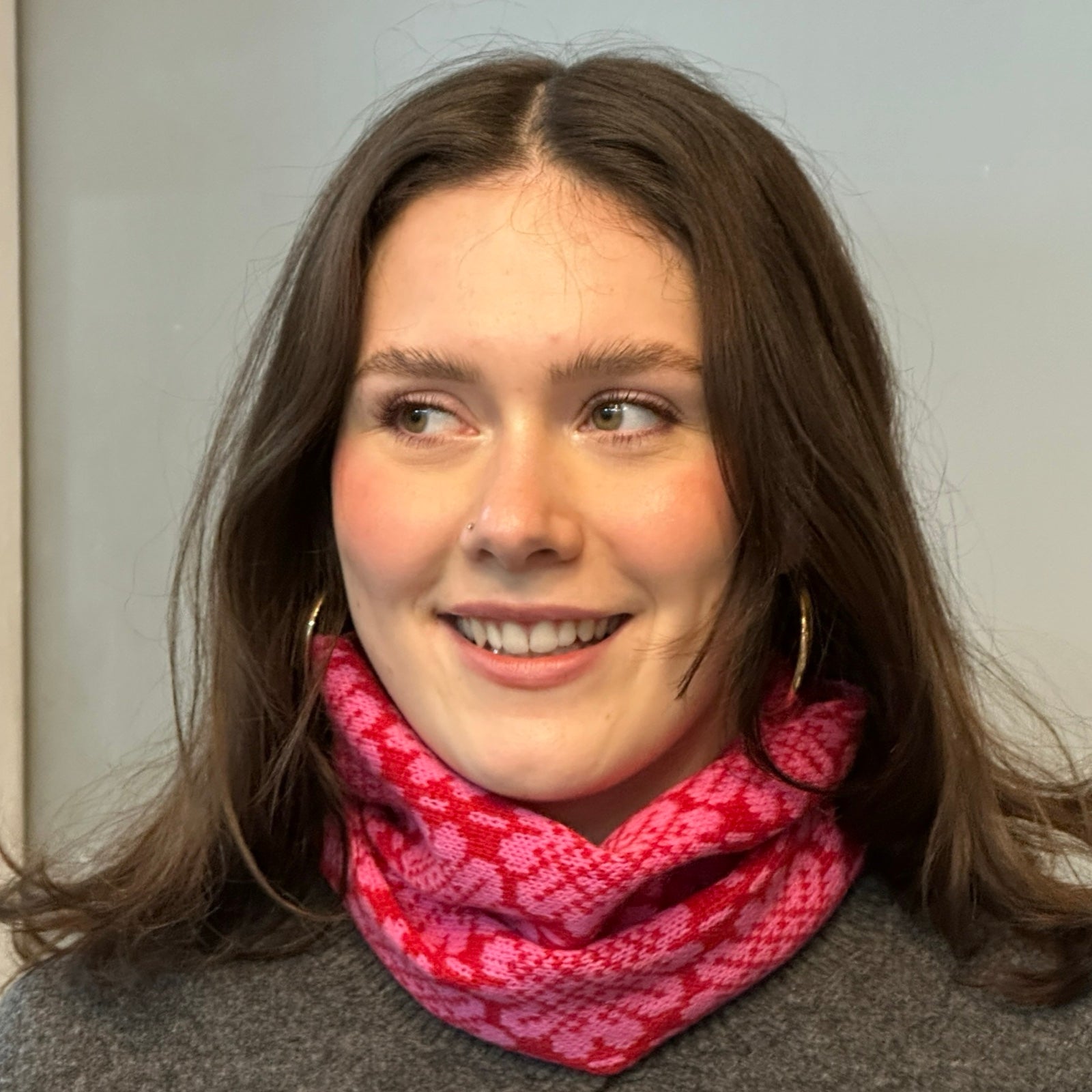 A soft and cosy 100% lambswool knitted snood in a pink daisy design against a red background.