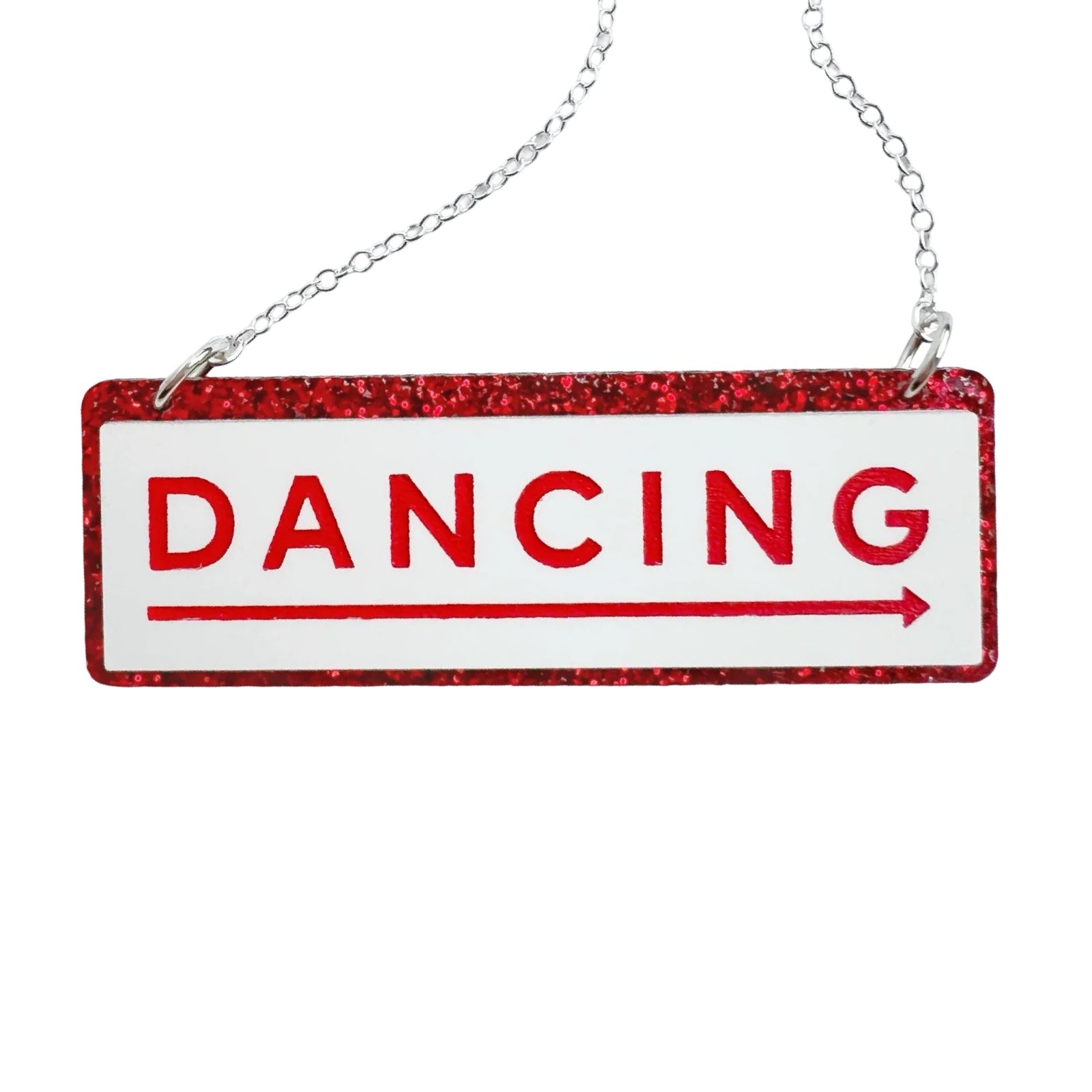 A necklace with a rectangular acrylic pendant with the word DANCING in red, with a long red arrow underneath in a white rectangle, all against a red glittery background. With a silver chain.