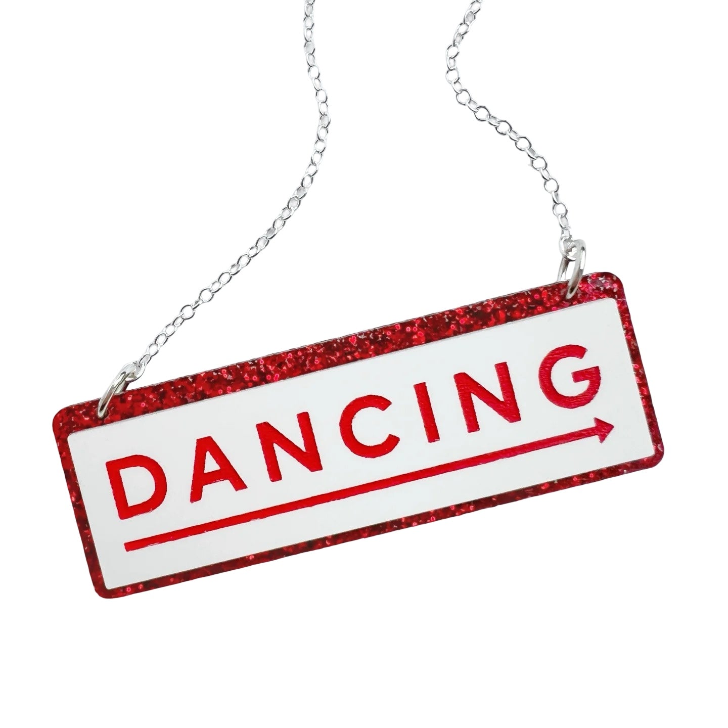 A necklace with a rectangular acrylic pendant with the word DANCING in red, with a long red arrow underneath in a white rectangle, all against a red glittery background. With a silver chain.