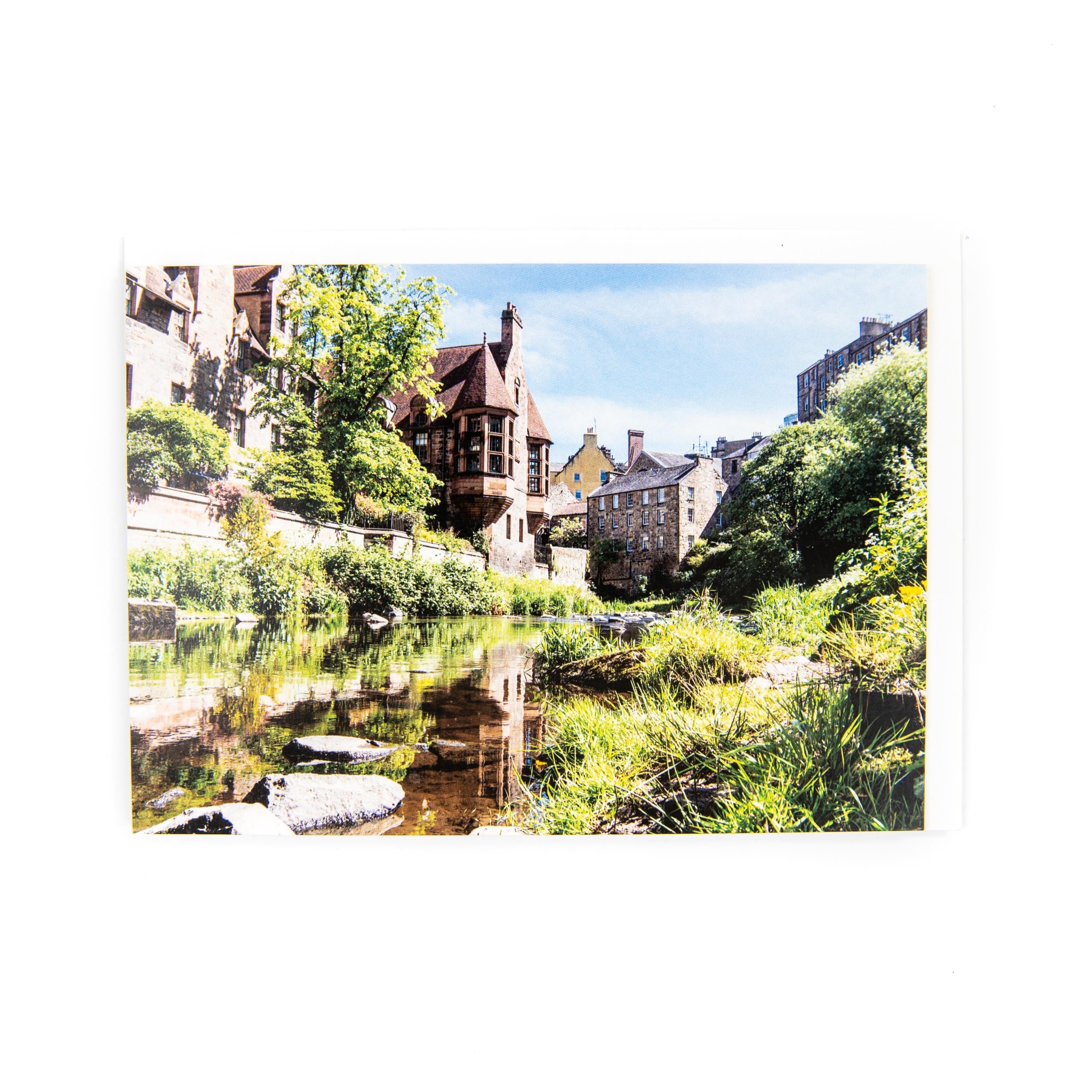 An A6 greeting card featuring a photograph of Dean Village, Edinburgh in summer. The card is blank inside and includes a white envelope.