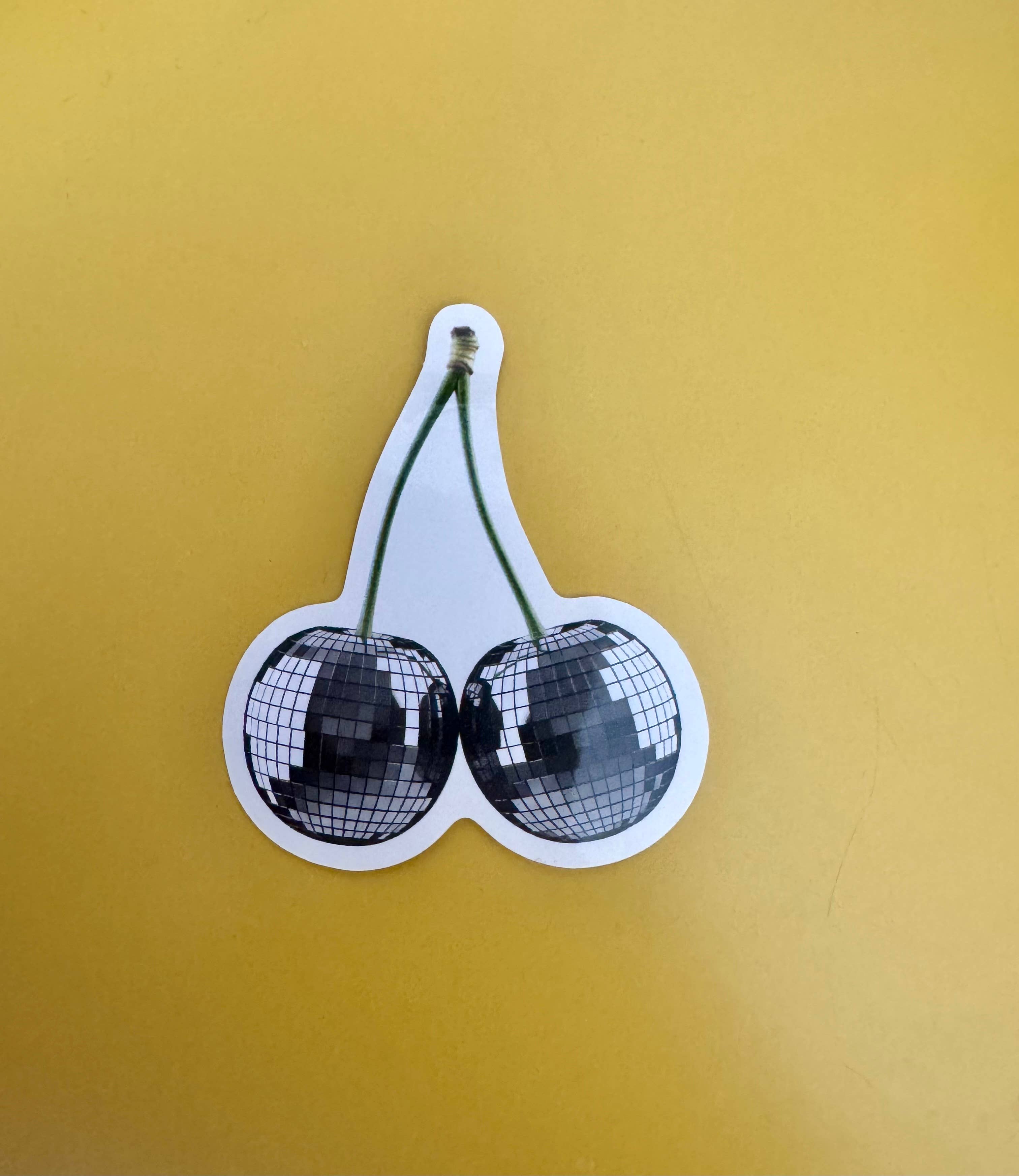 A waterproof vinyl sticker of a pair of cherries with disco balls instead of berries, on a yellow background.