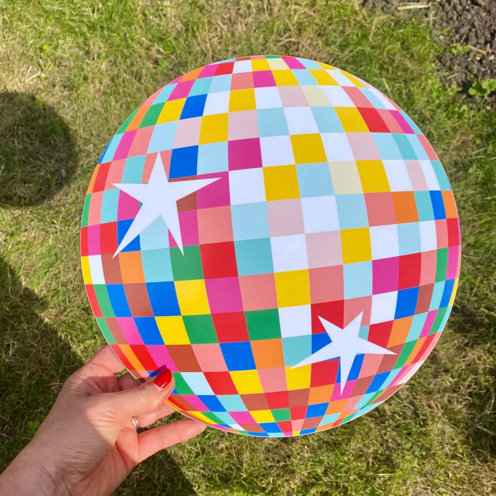 Colourful disco ball with star patterns held by a hand on grass.