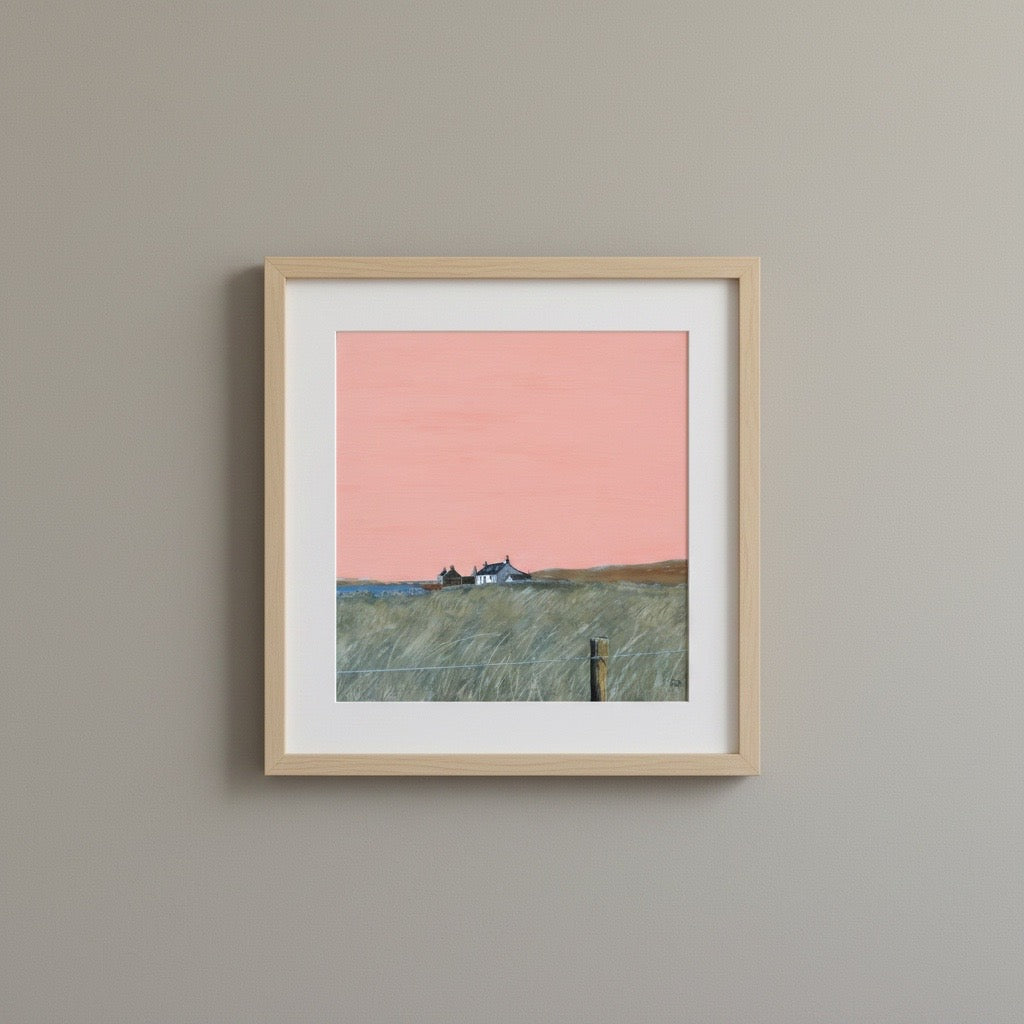 A framed landscape art print featuring a pink sky and a grassy field with a small house, mounted on a light gray wall.