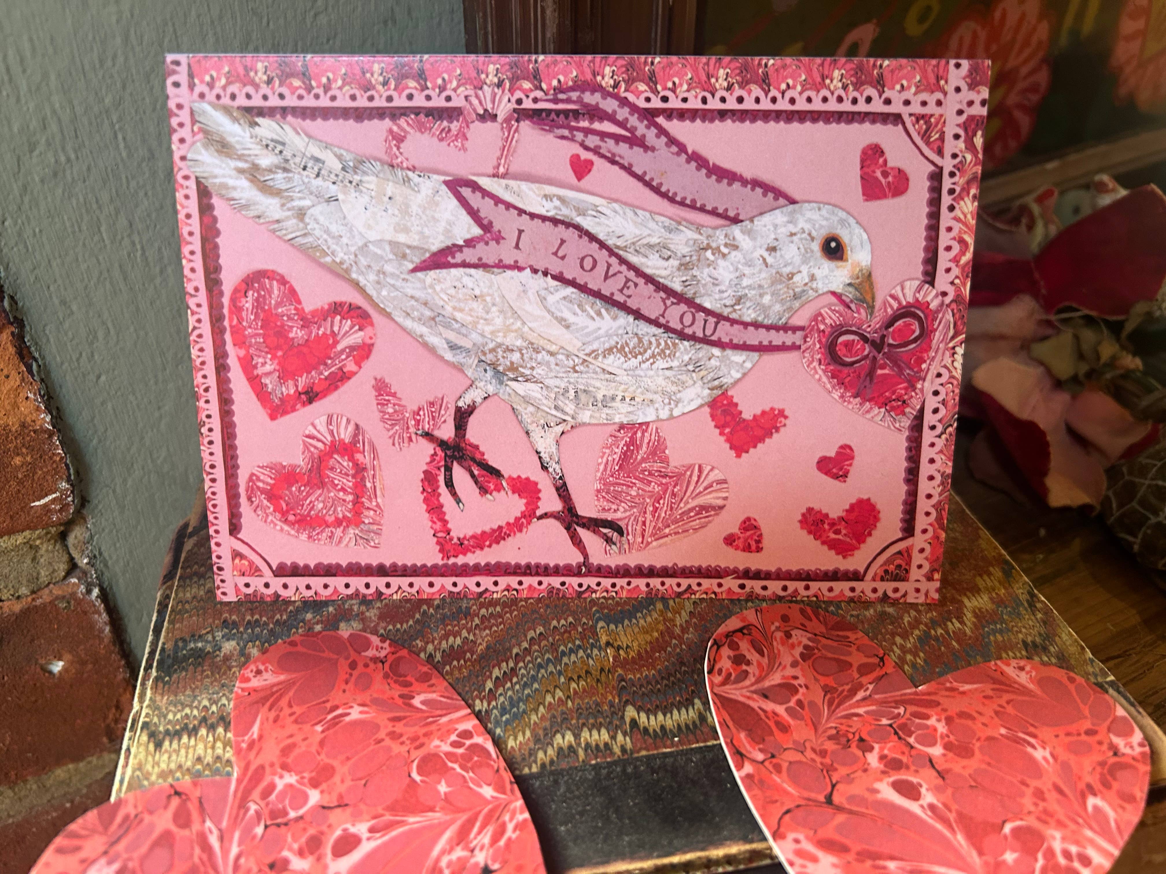 Pink card with a bird and heart designs on a textured surface.