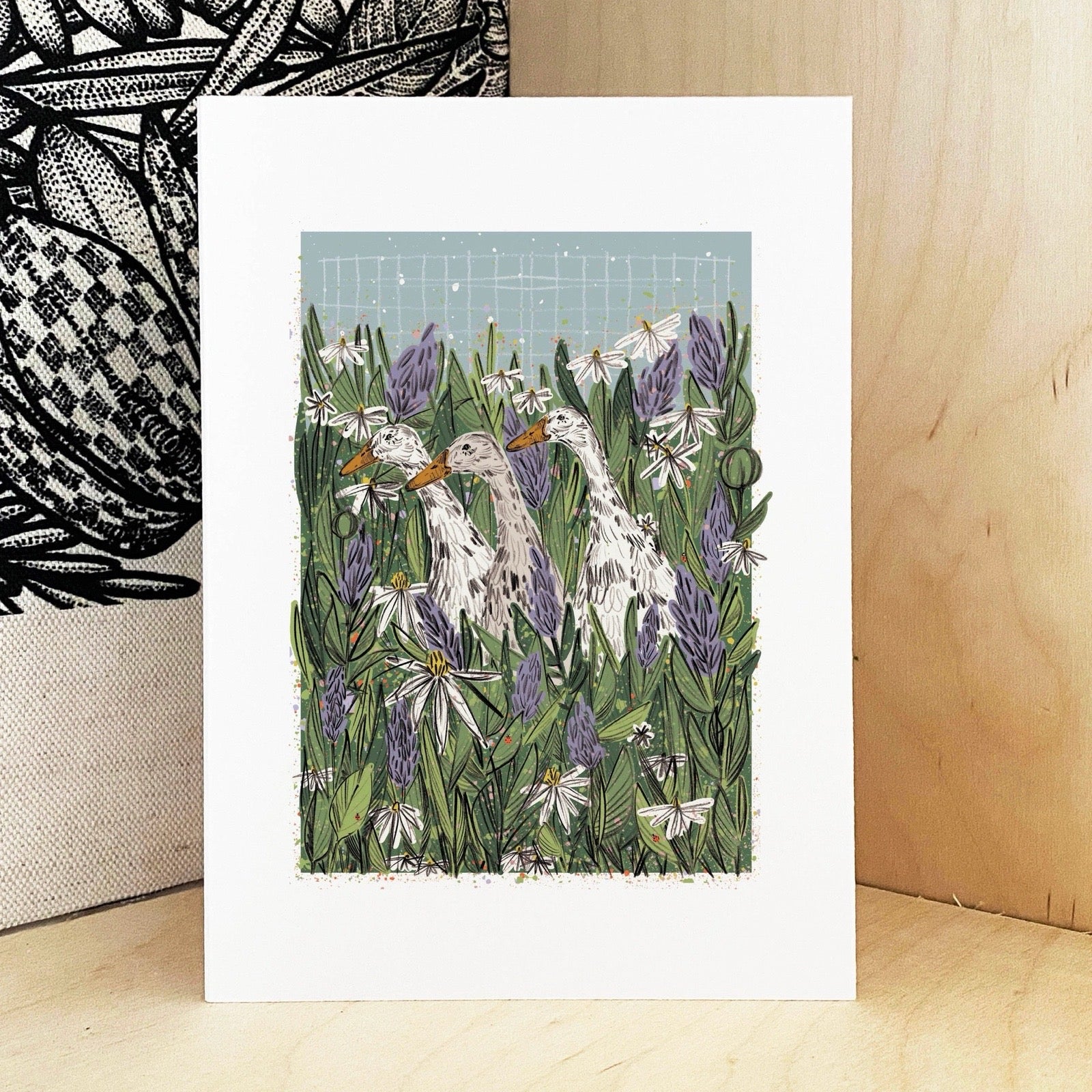 Art print of three duck among green foliage and purple flowers on a wooden surface.