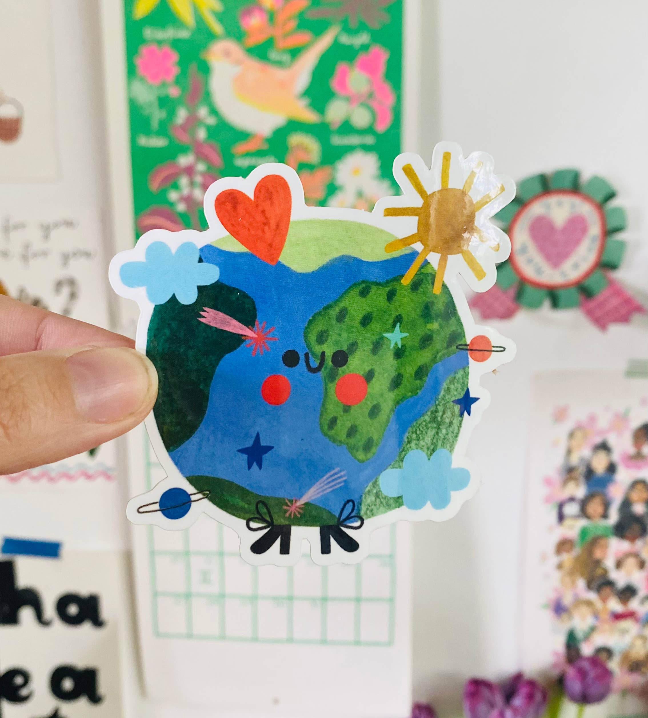 Colorful sticker of a smiling Earth with hearts, flowers, and a sun held by a hand.