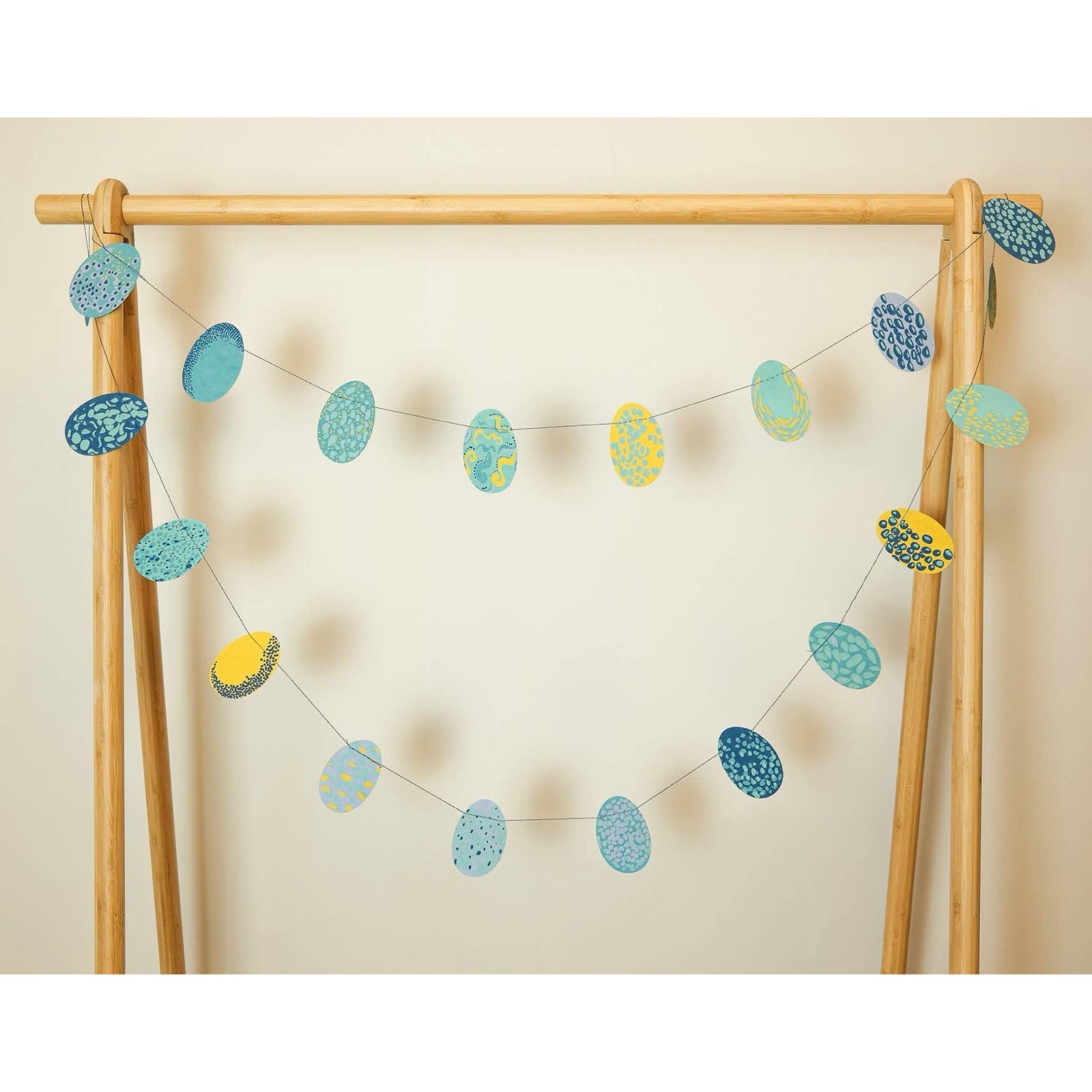 Easter egg paper garland (with 20 eggs) in various shades of blue and yellow hanging from a wooden frame.