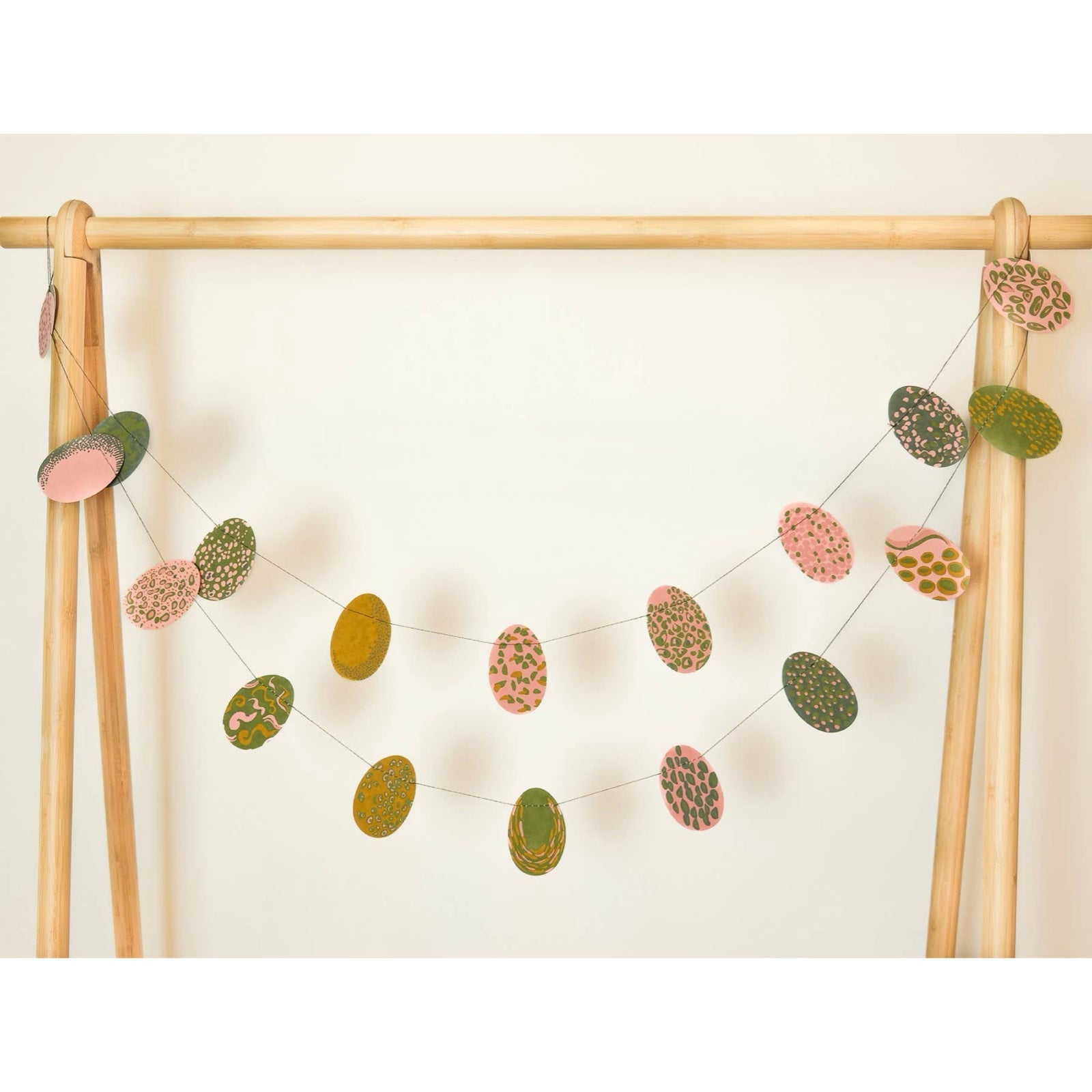 Easter egg paper garland (with 20 eggs) in various shades of pink and green hanging from a wooden frame.