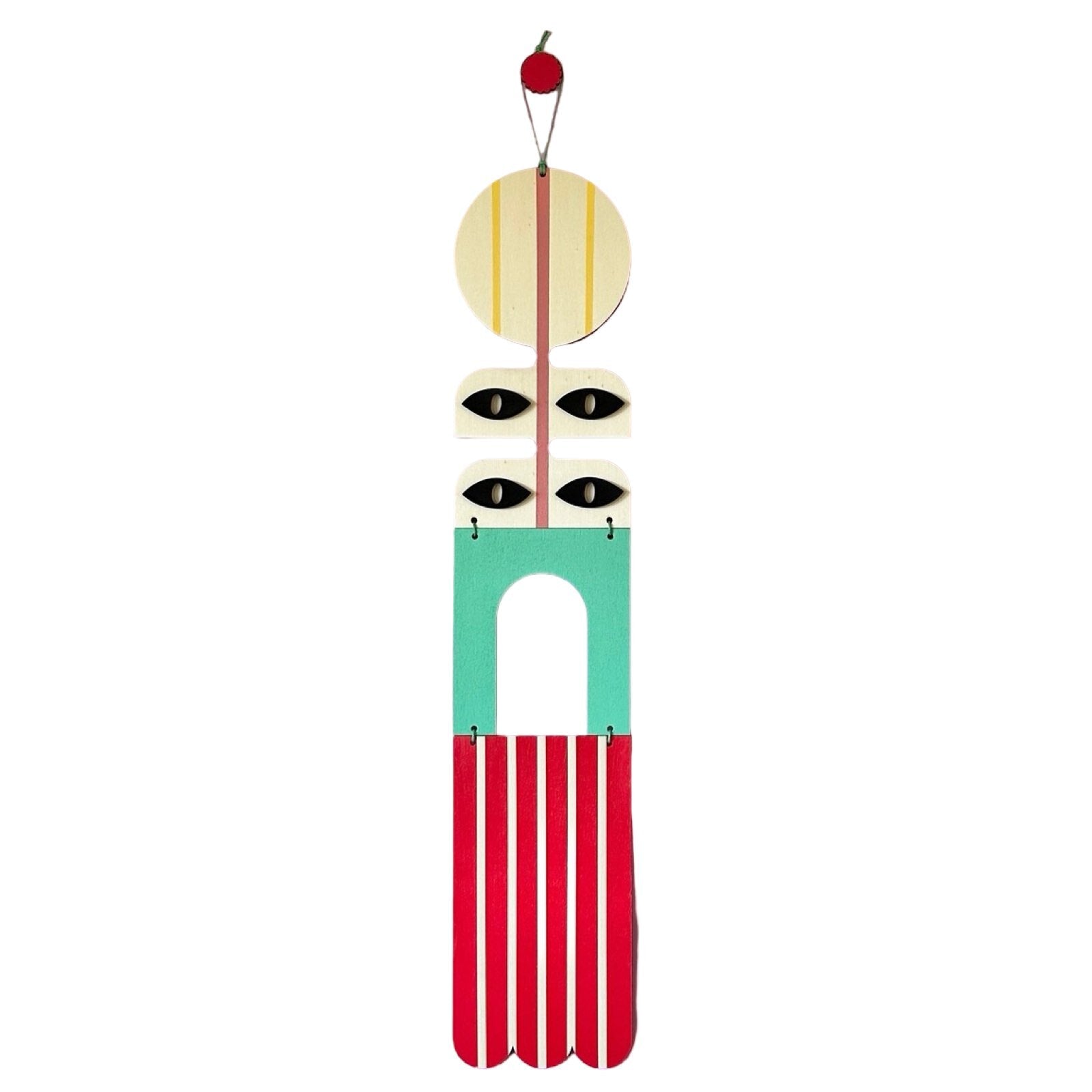A geometric modern wall art hanging in red, green, black, and white with a waxed cord and wooden beads.