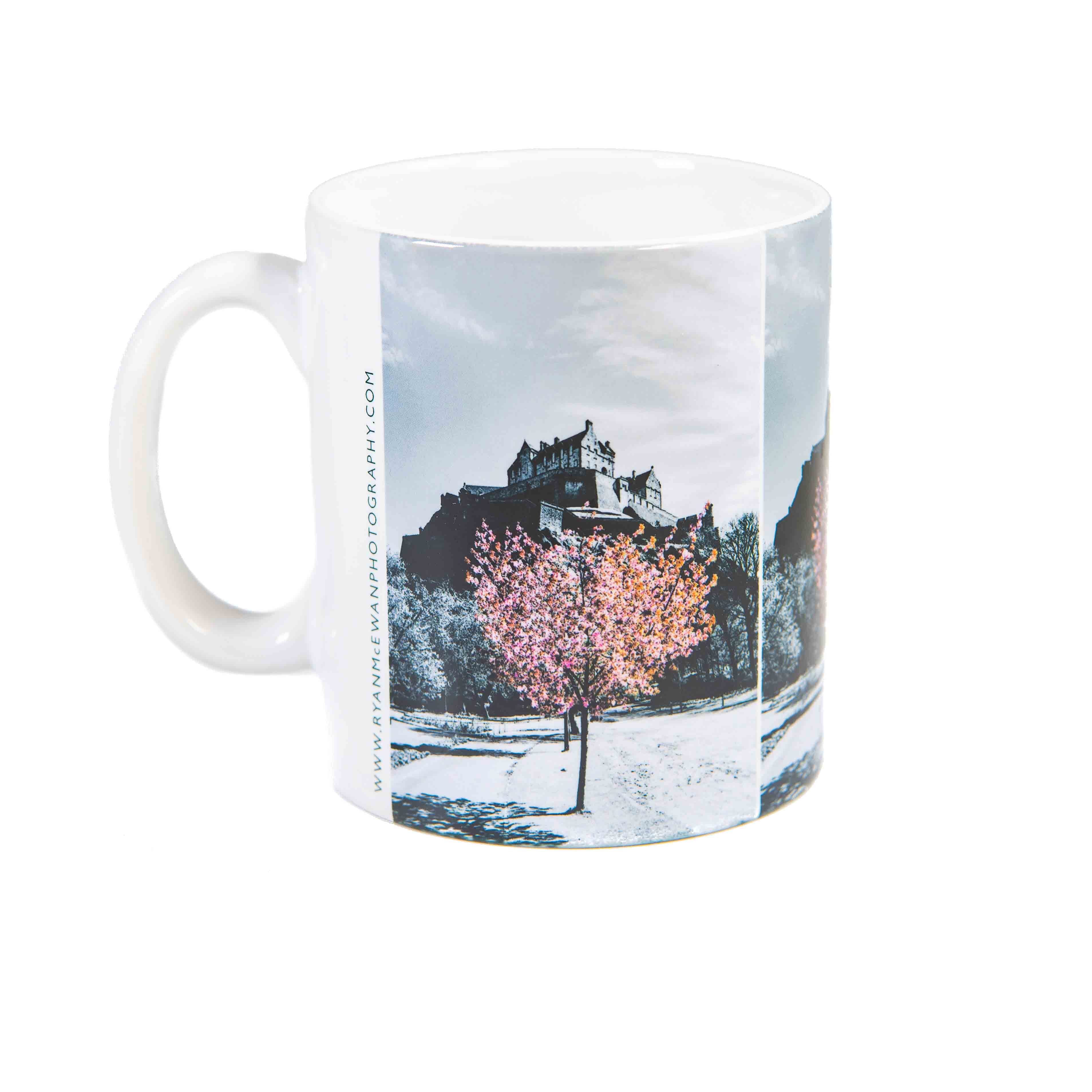 An image of a mug with a picture of Edinburgh castle on it with a tree featuring pink blossom.