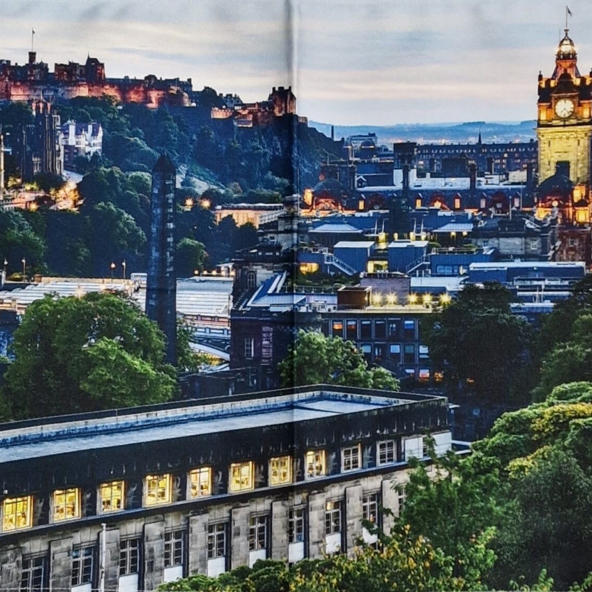 Edinburgh cityscape at dusk with illuminated buildings and clock tower.