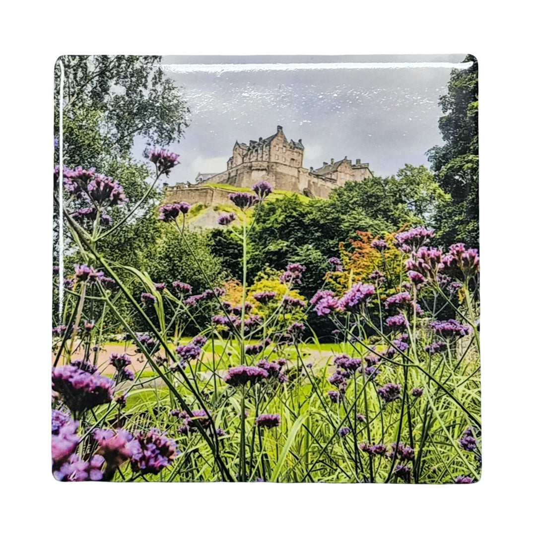 Castle surrounded by greenery and purple flowers on a ceramic coaster.
