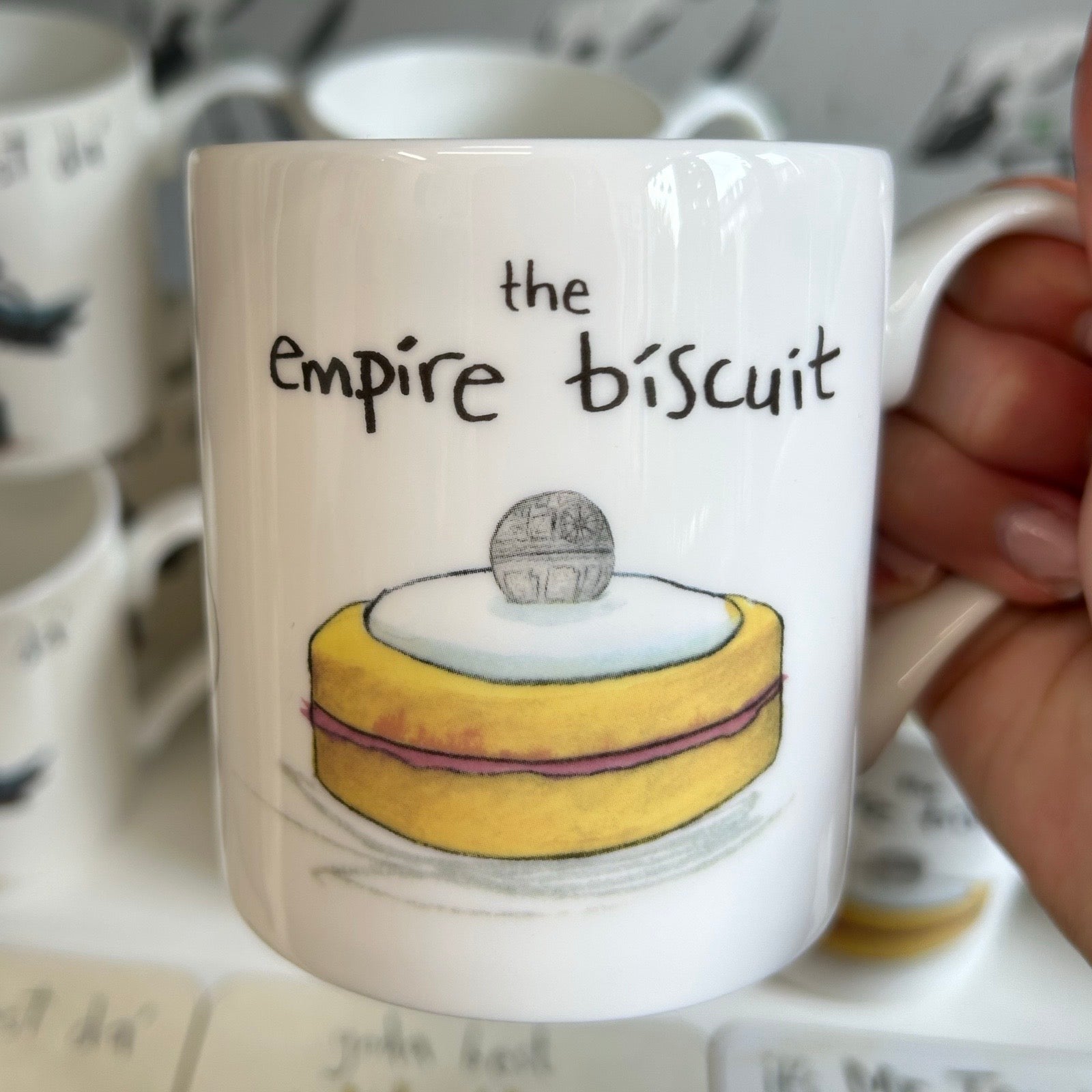 Mug with 'the empire biscuit' design held by a hand, with blurred background.