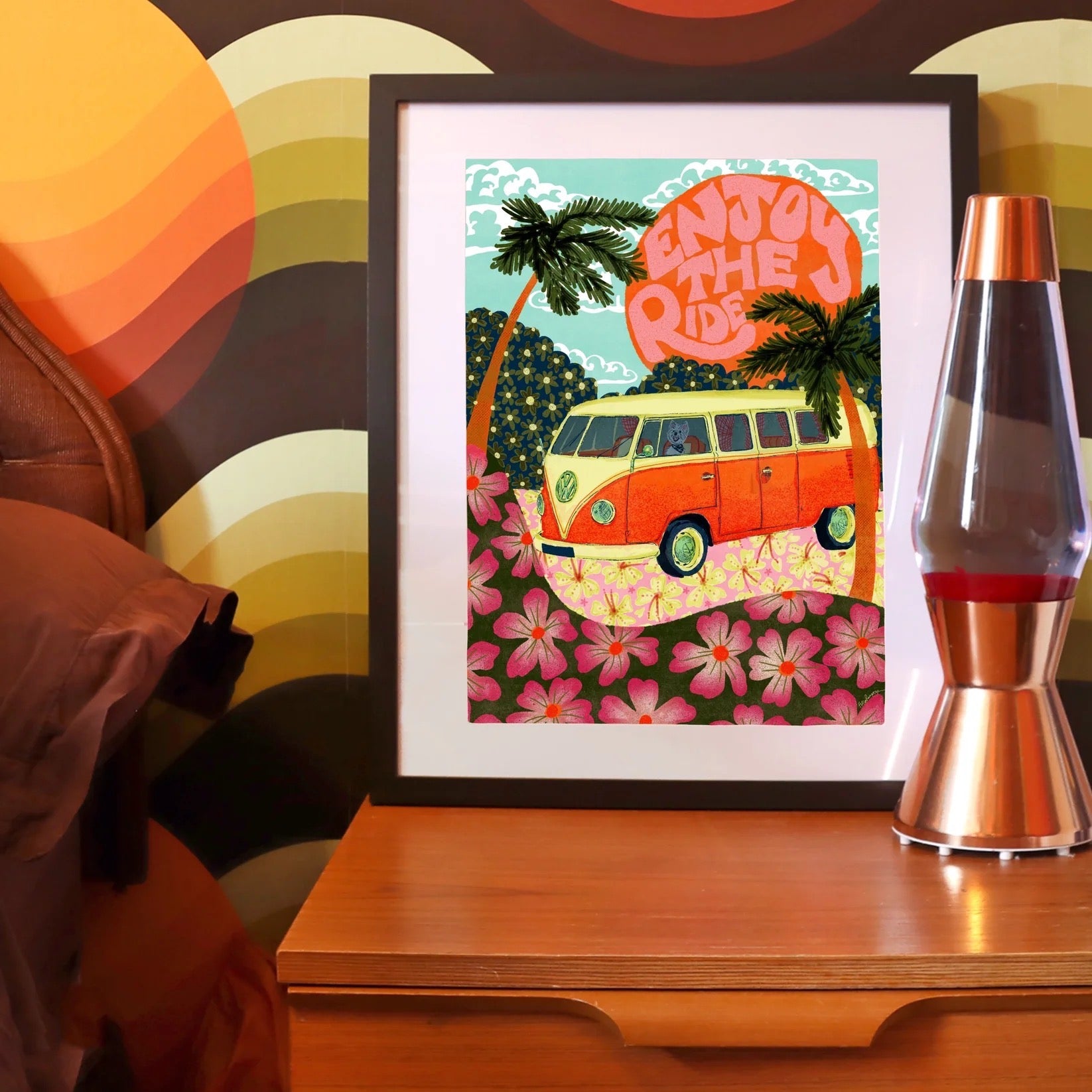 Framed artwork with a van and palm trees on a wooden surface with a colorful abstract background.