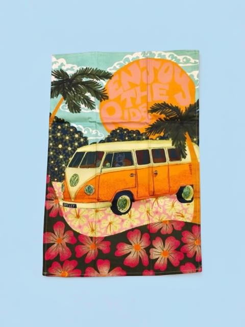 Notebook with a retro van, palm trees, and flowers on a colourful tea towel against a blue background.