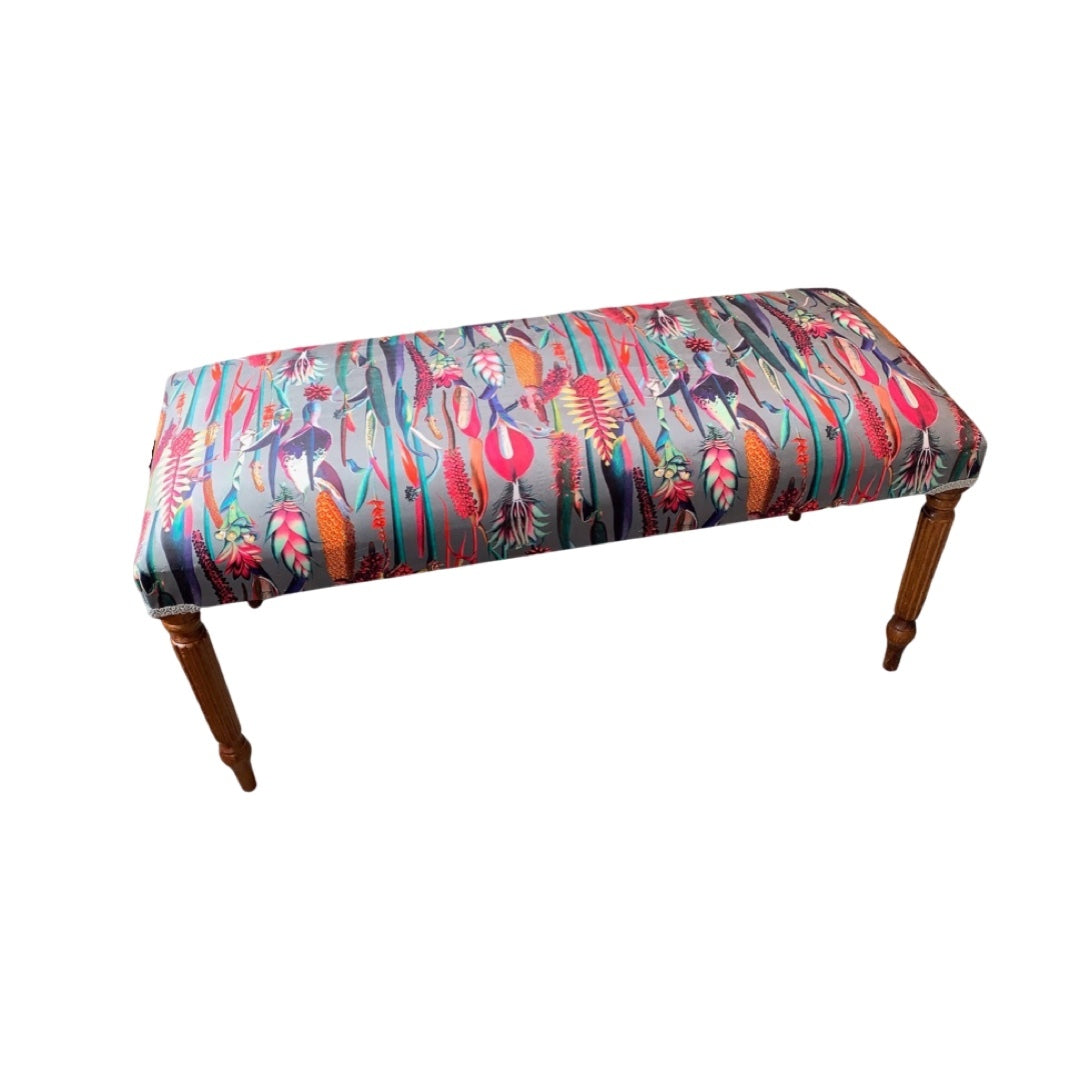 A rectangular bench covered in grey velvet fabric with a colorful exotic flower design, featuring mahogany legs.