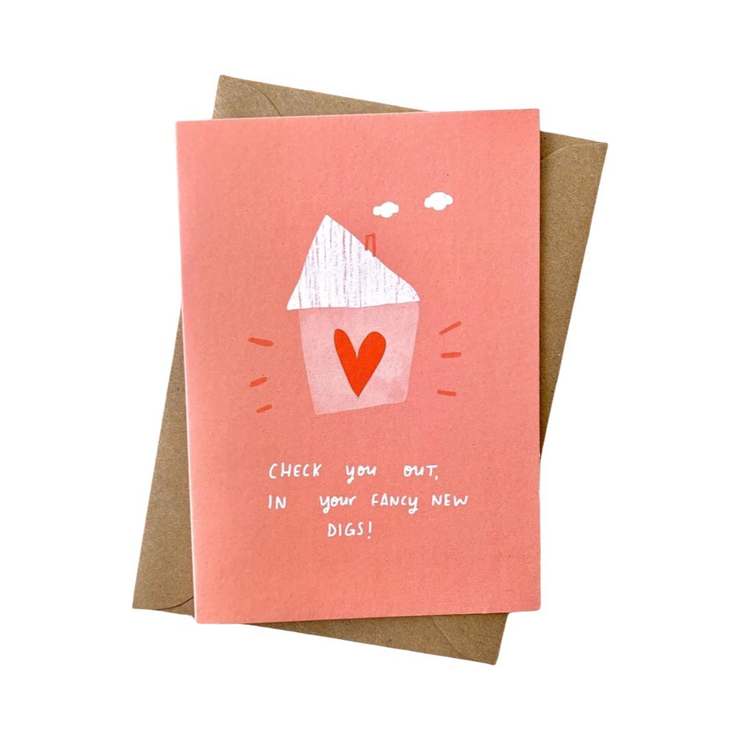 A greeting card with a pink background, featuring a small white house with a red heart, and the text 'Check you out, in your fancy new digs!' in white.
