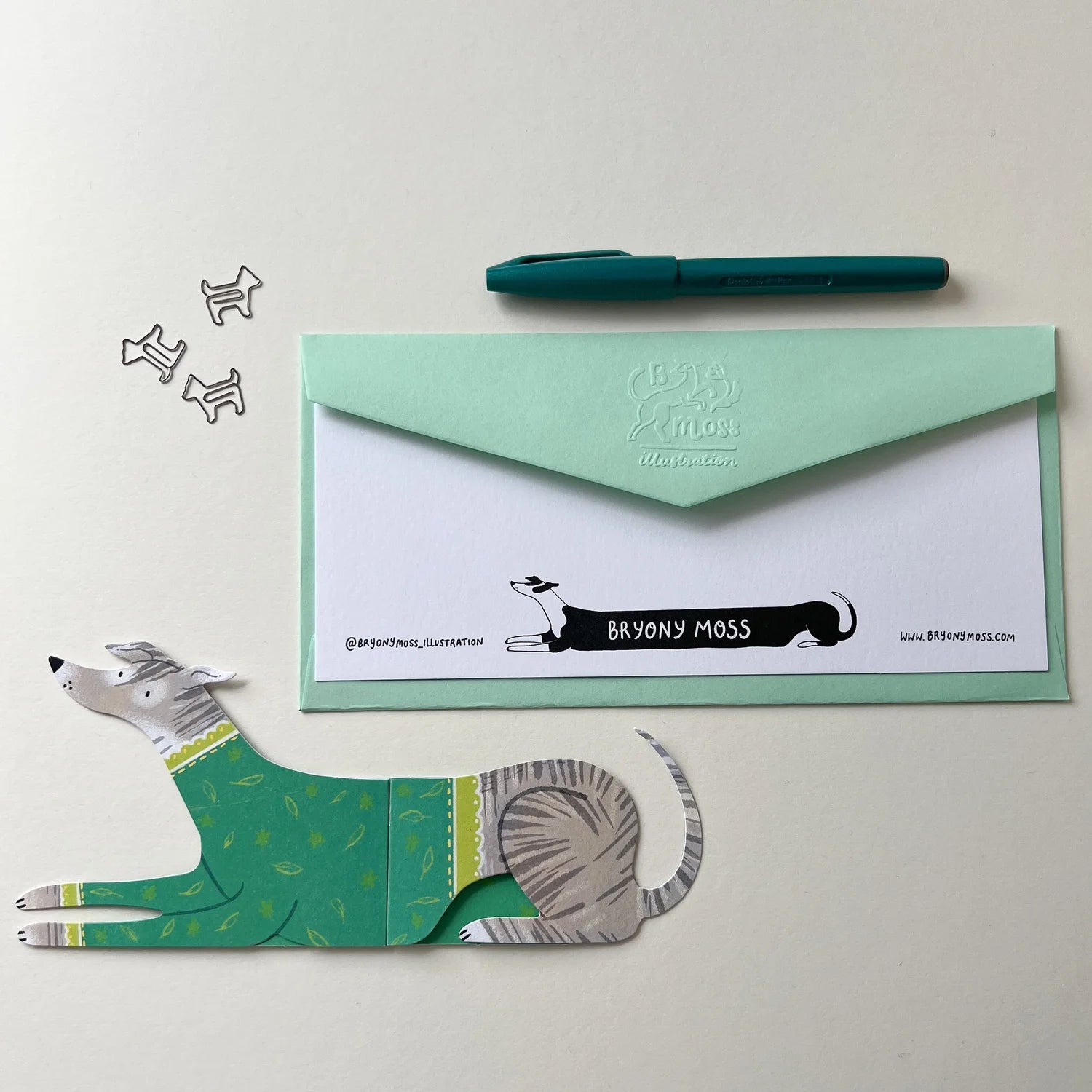 Green dog-shaped card with envelope and pen on a light grey background.