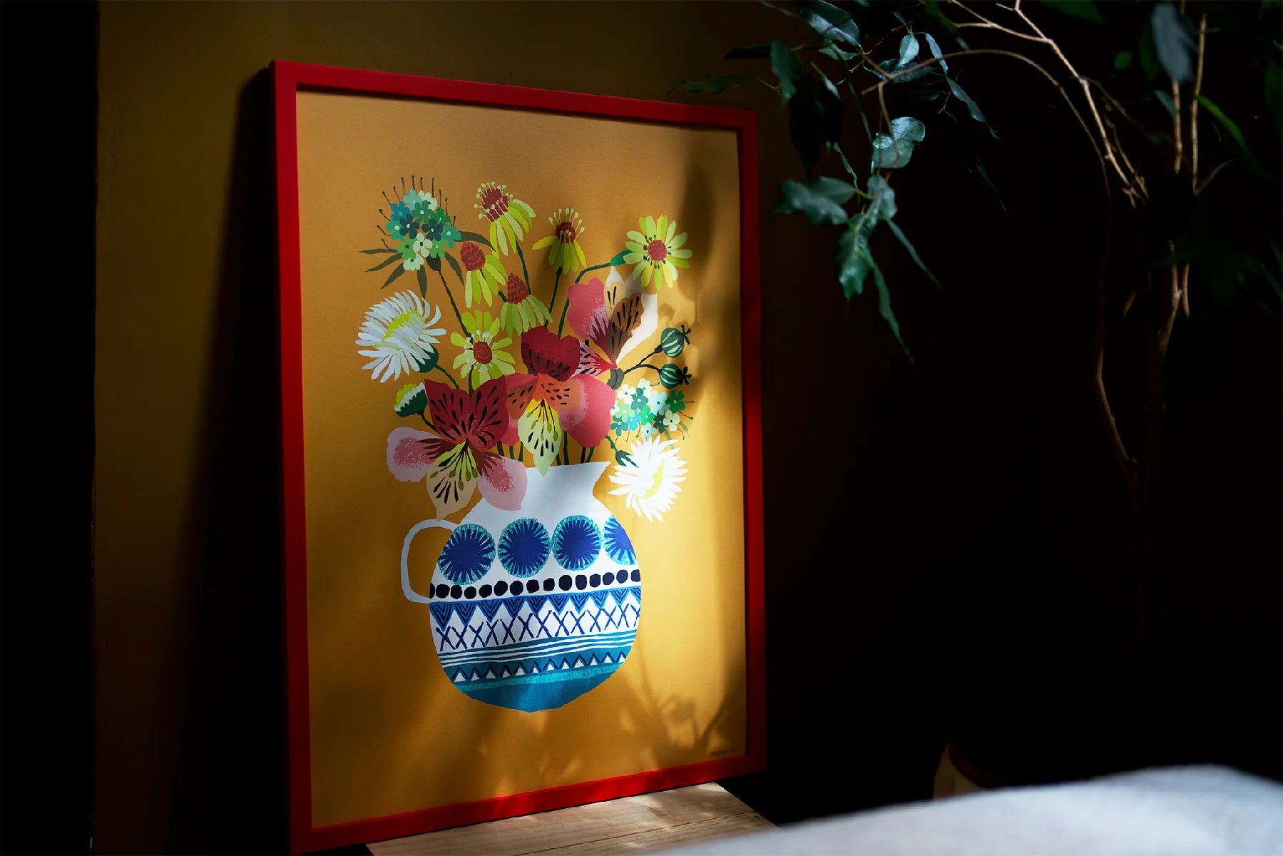 Framed artwork of a colorful floral arrangement in a blue and white vase on a yellow background.