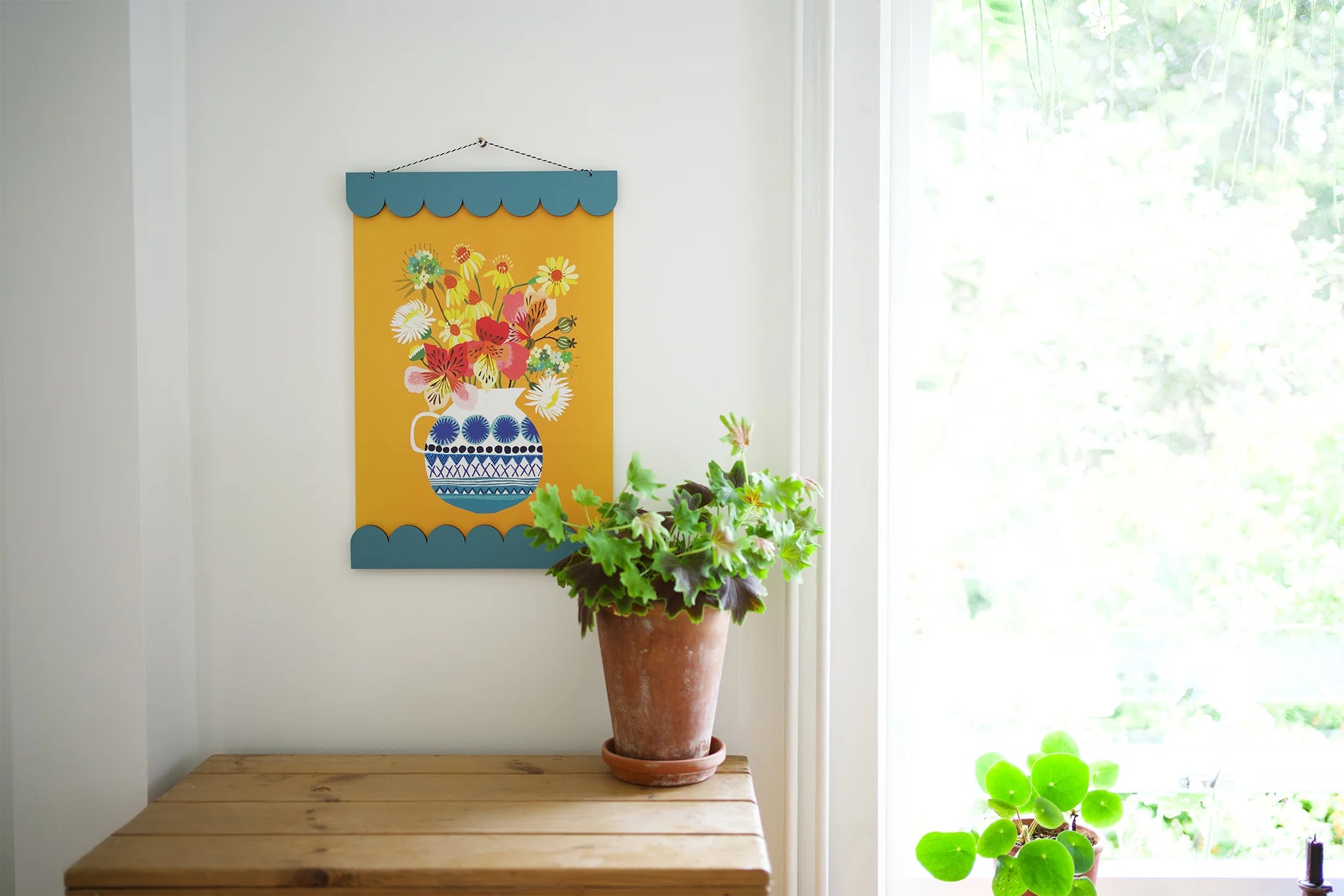 Decorative wall hanging with floral design by a wooden table, by a window.