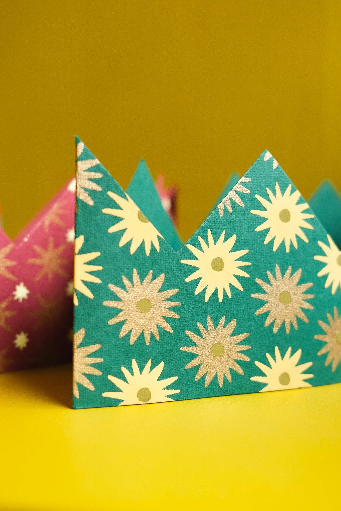 Teal paper crown with yellow floral pattern on a yellow background.