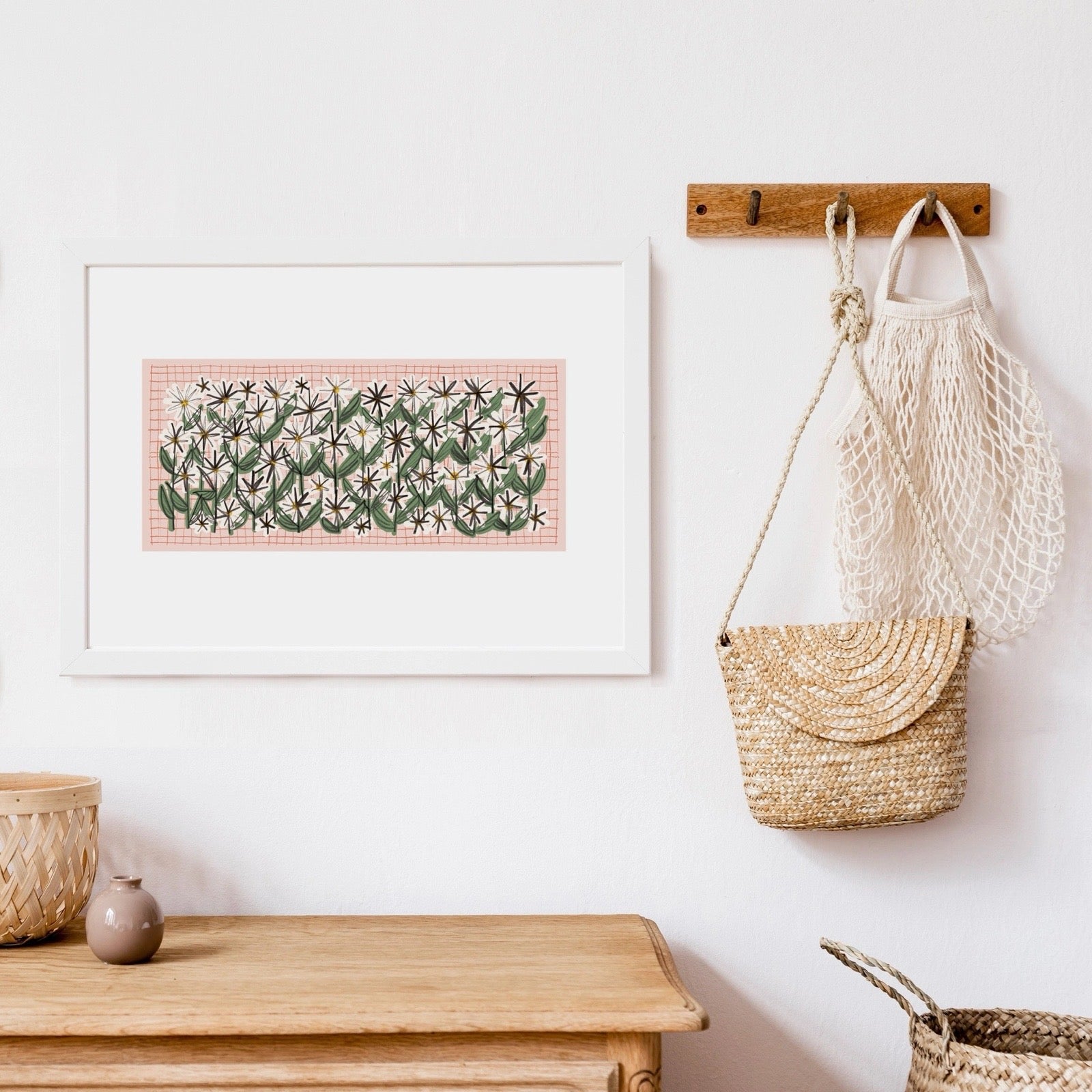 Framed artwork on a wall with woven baskets on a shelf and a bag hanging on hooks.