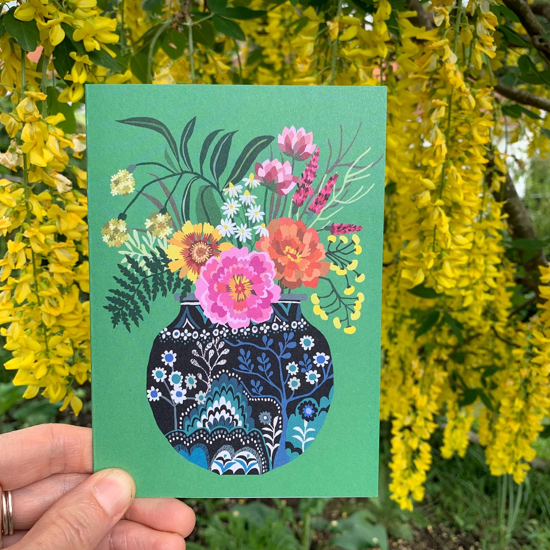 Card with floral design held in front of yellow flowers.