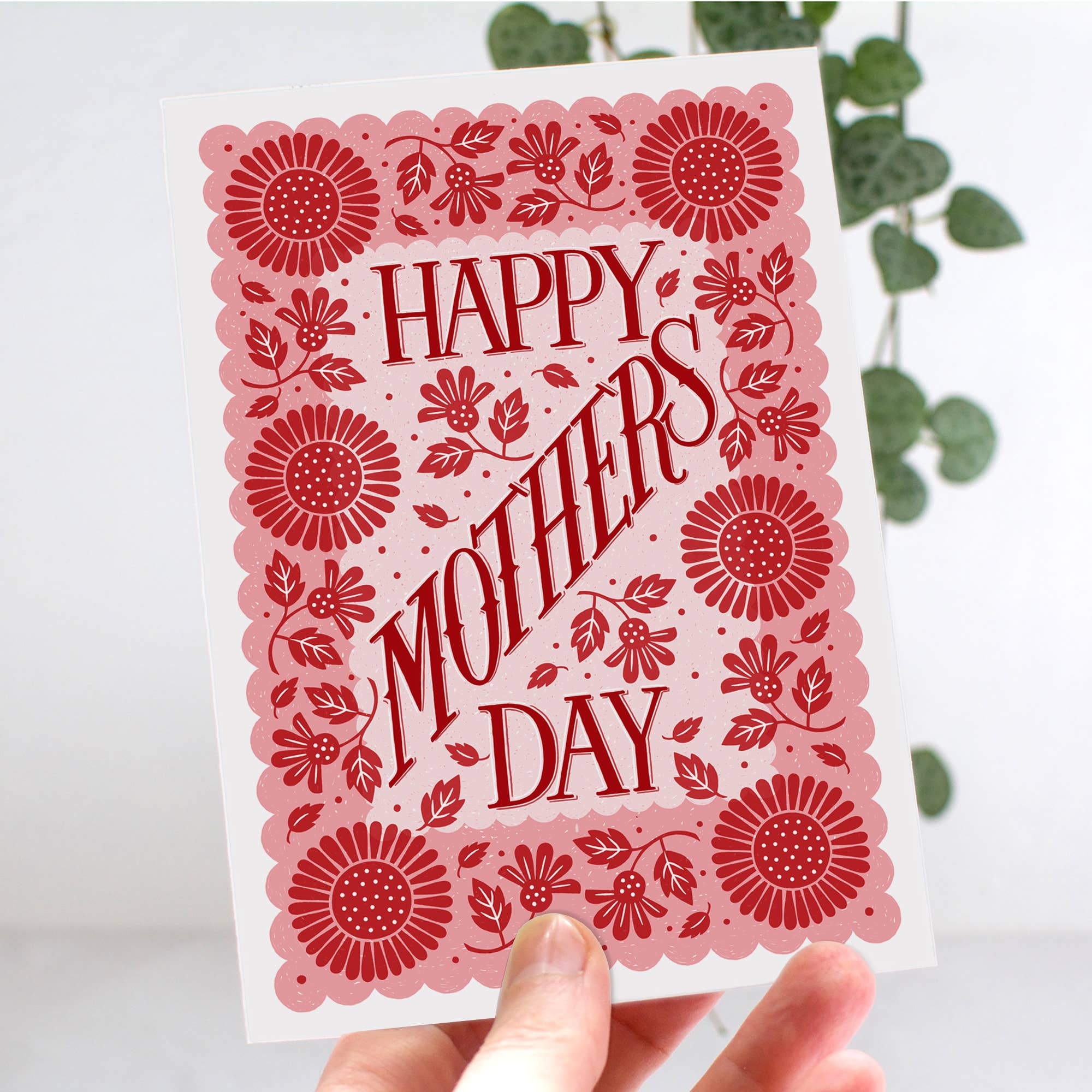 Card with 'Happy Mother's Day' text and red floral patterns held against a light background.