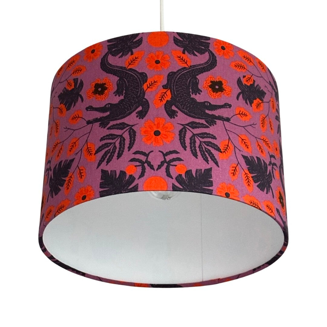 Close up of a drum lampshade in purple cotton with navy alligators and leaves and orange flowers.