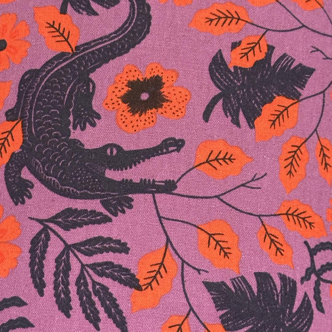 Purple fabric with navy alligators and leaves and orange flowers.