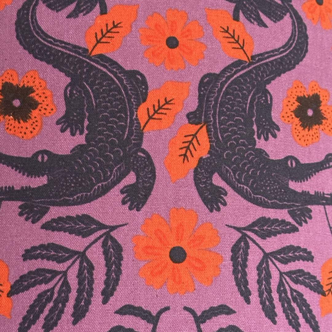 Purple fabric with navy alligators and leaves and orange flowers.