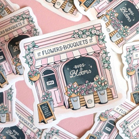 A sticker featuring an illustration of a beautiful flower shop with a pink and white striped awning and flowers at the front in vases.