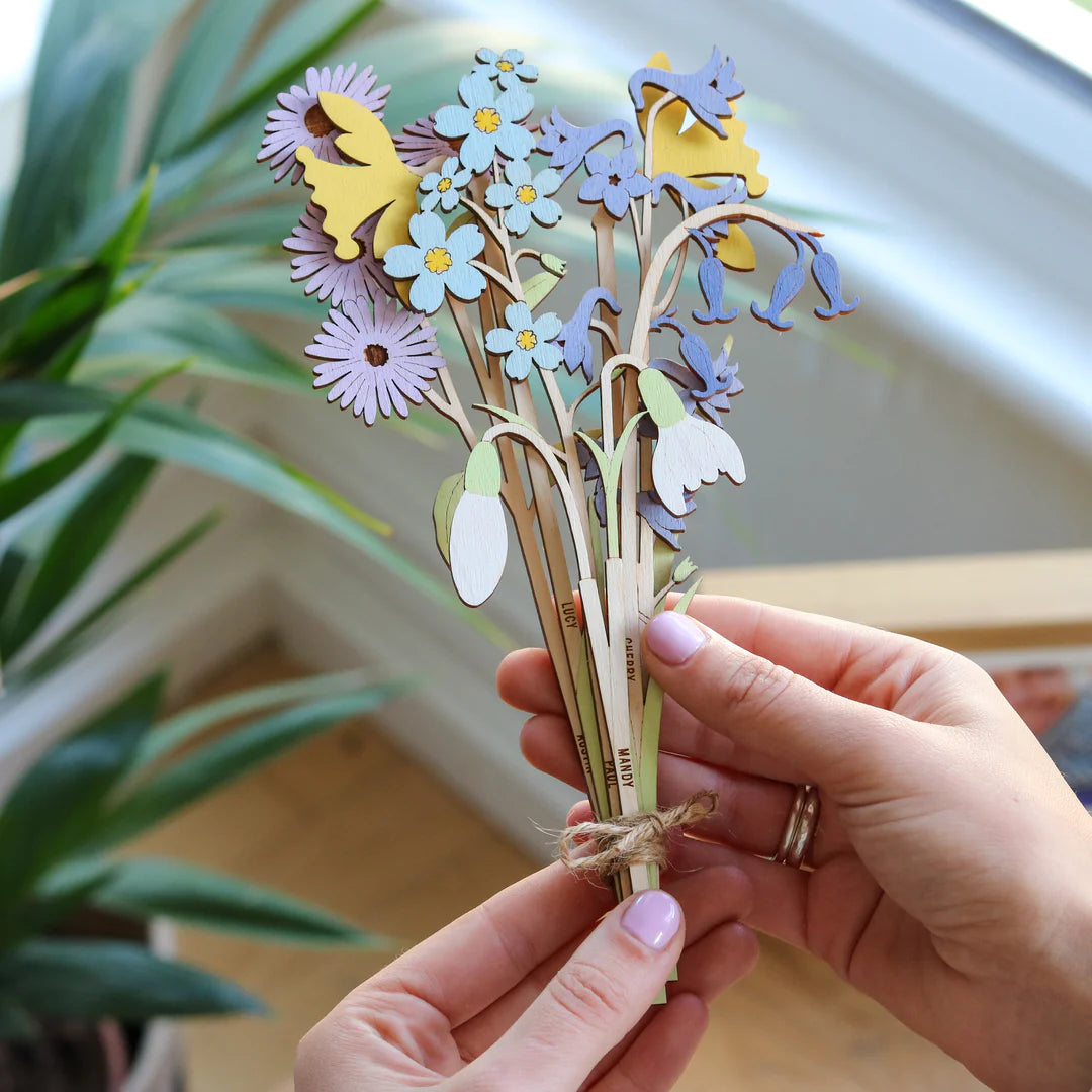 Hand holding a bouquet of colourful wooden flowers with a blurred indoor background.