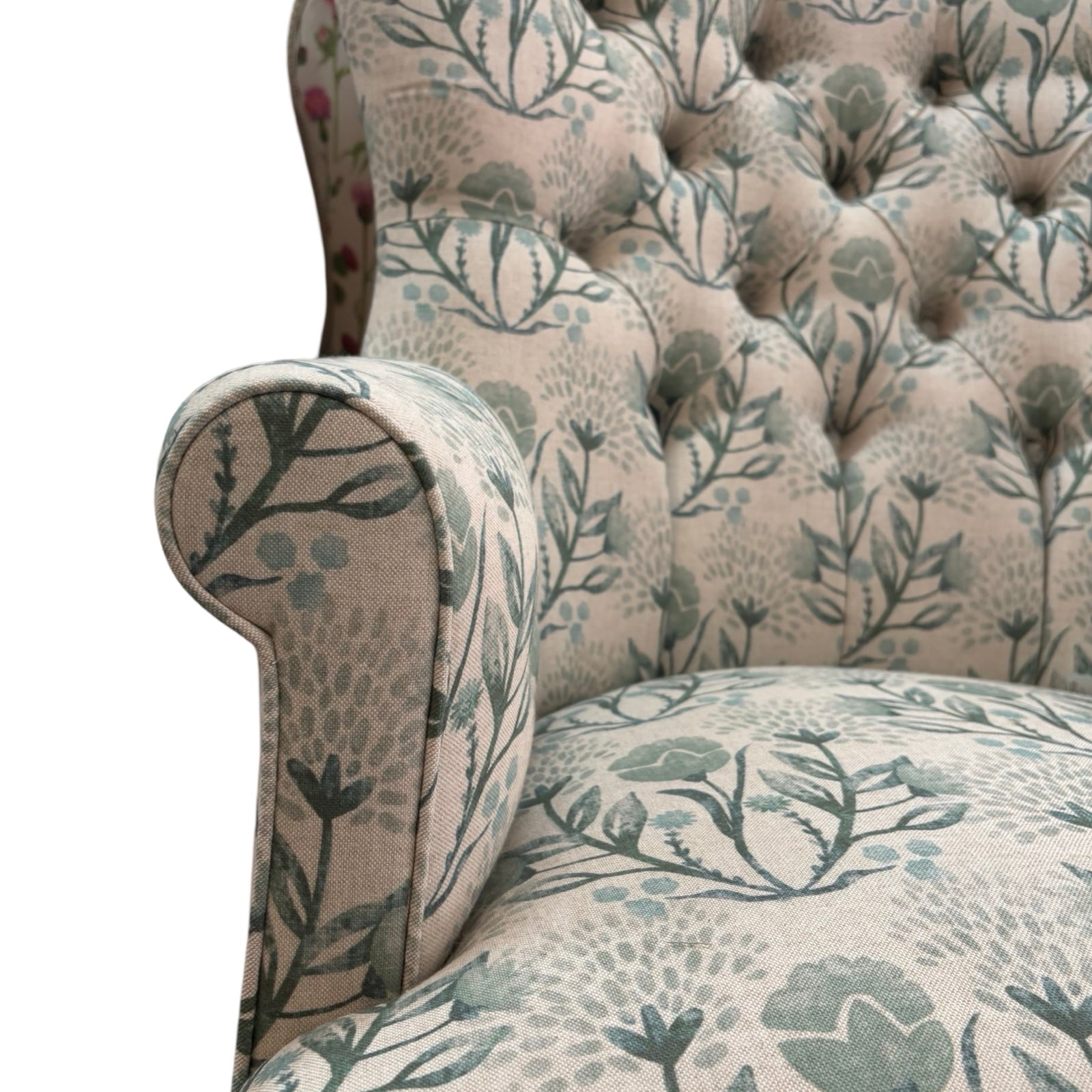 The arm detail of an occasional armchair in cream linen fabric with flowers in soft blues and greens and finished with cream binding, mahogany stained legs and gold coloured castors.