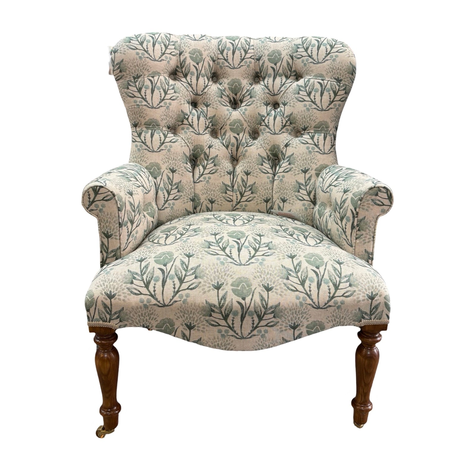 An occasional armchair in cream linen fabric with flowers in soft blues and greens and finished with cream binding, mahogany stained legs and gold coloured castors.