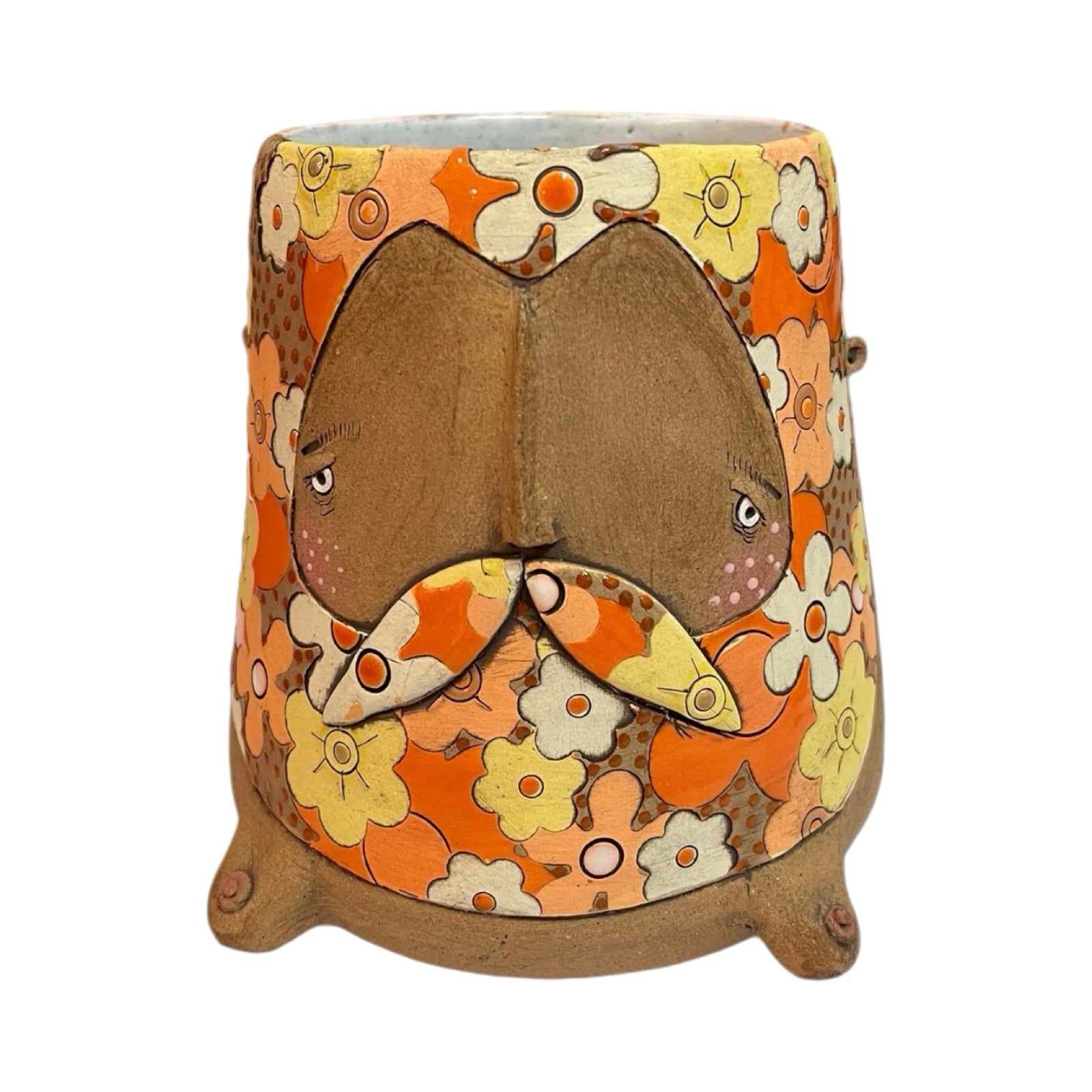A ceramic beaker with a male moustached face and a white, orange, yellow and brown retro-inspired floral pattern.