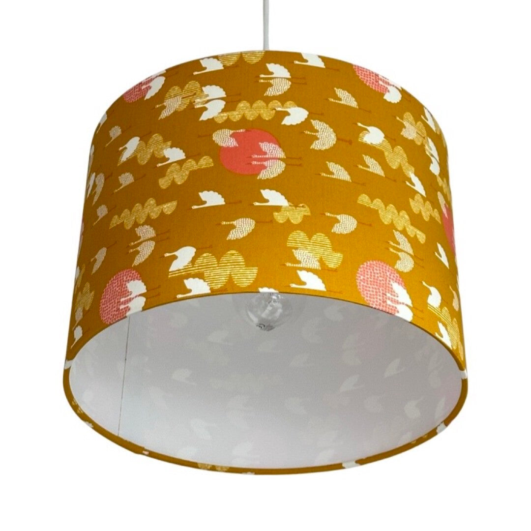 Close up of a drum lampshade covered in mustard cotton fabric with white birds and pink moons