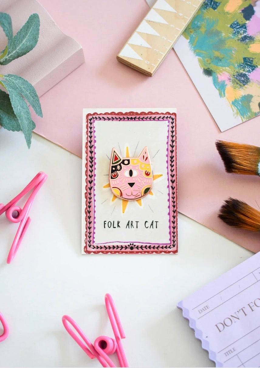 Folk cat badge on a desk with stationery items.