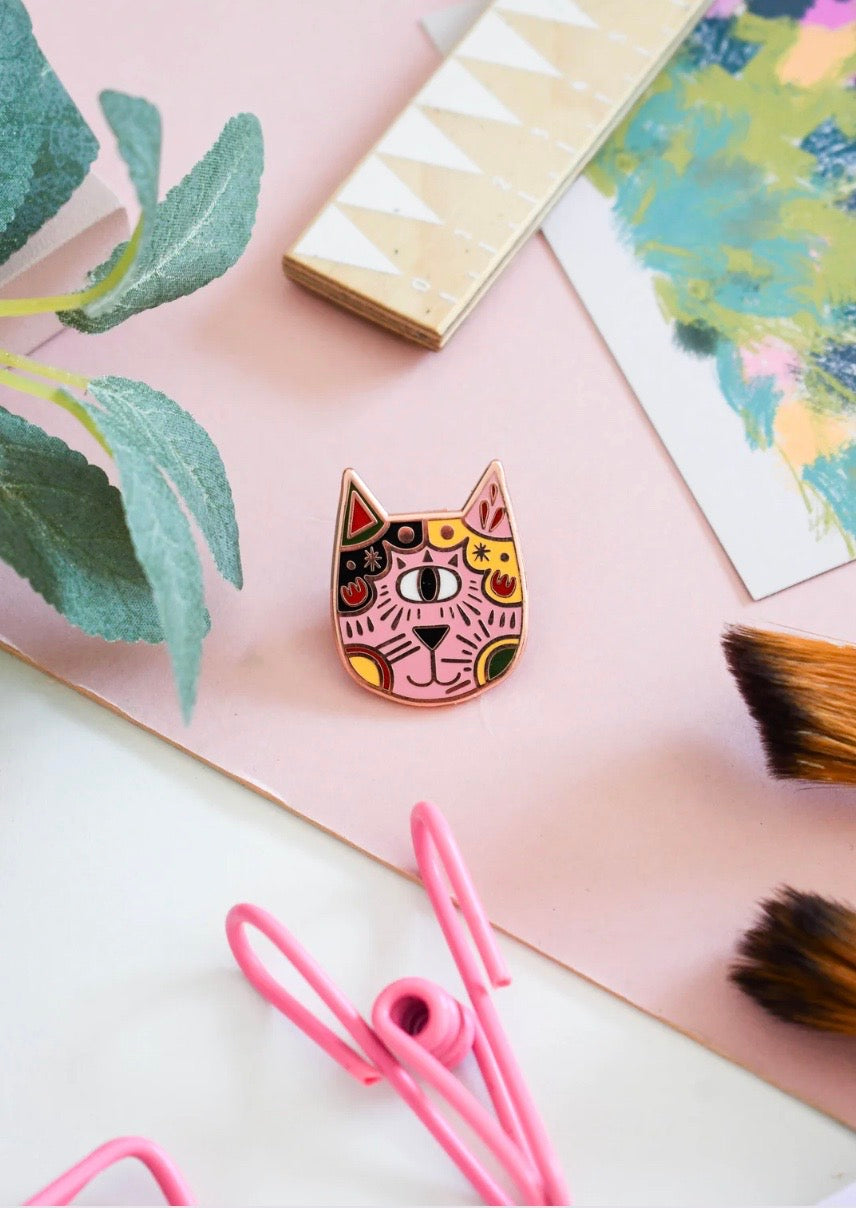 Colourful cat-shaped badge on a pink surface with decorative elements.
