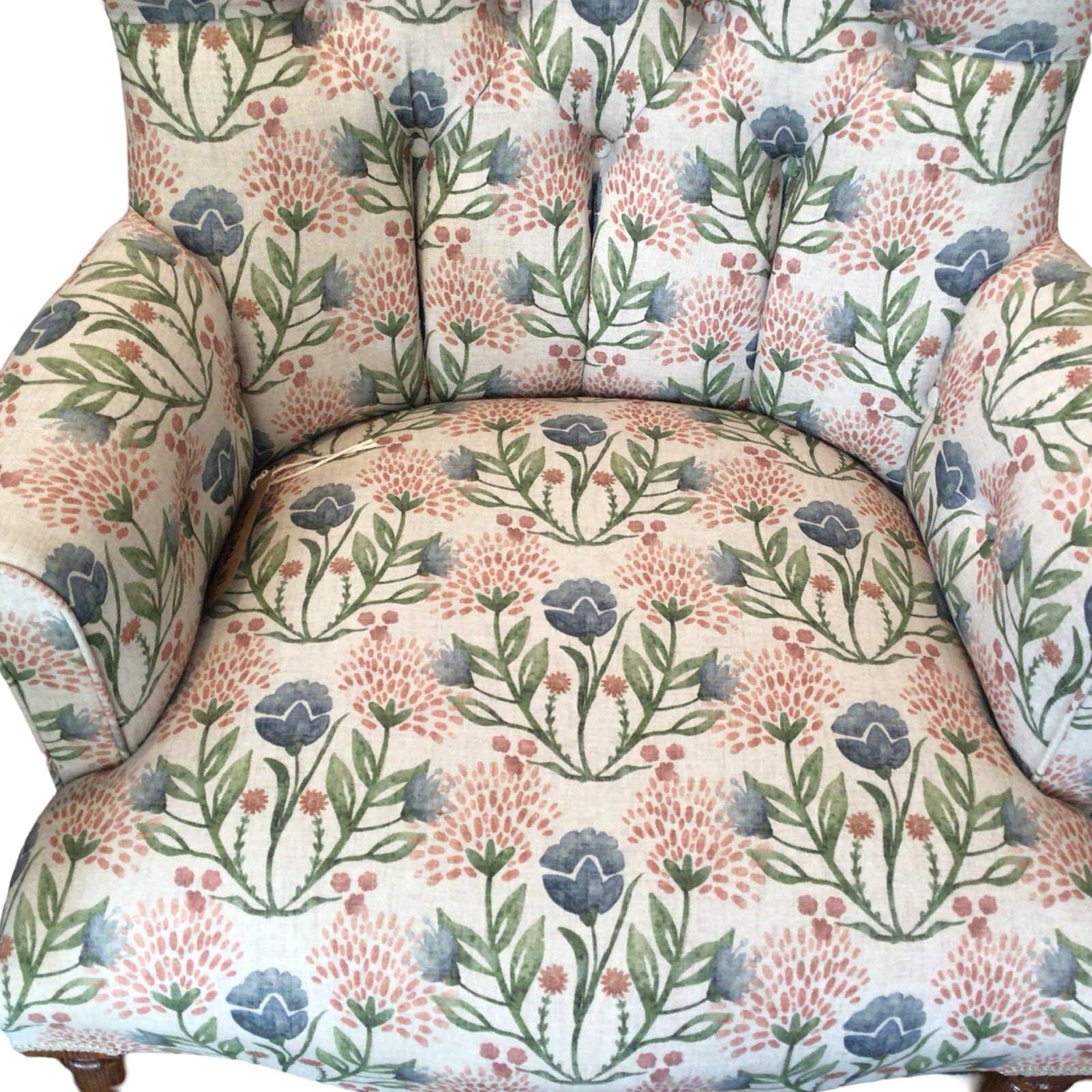A cream linen armchair with pink and pale blue floral pattern, featuring mahogany legs and gold castors, upholstered with a button-back design.