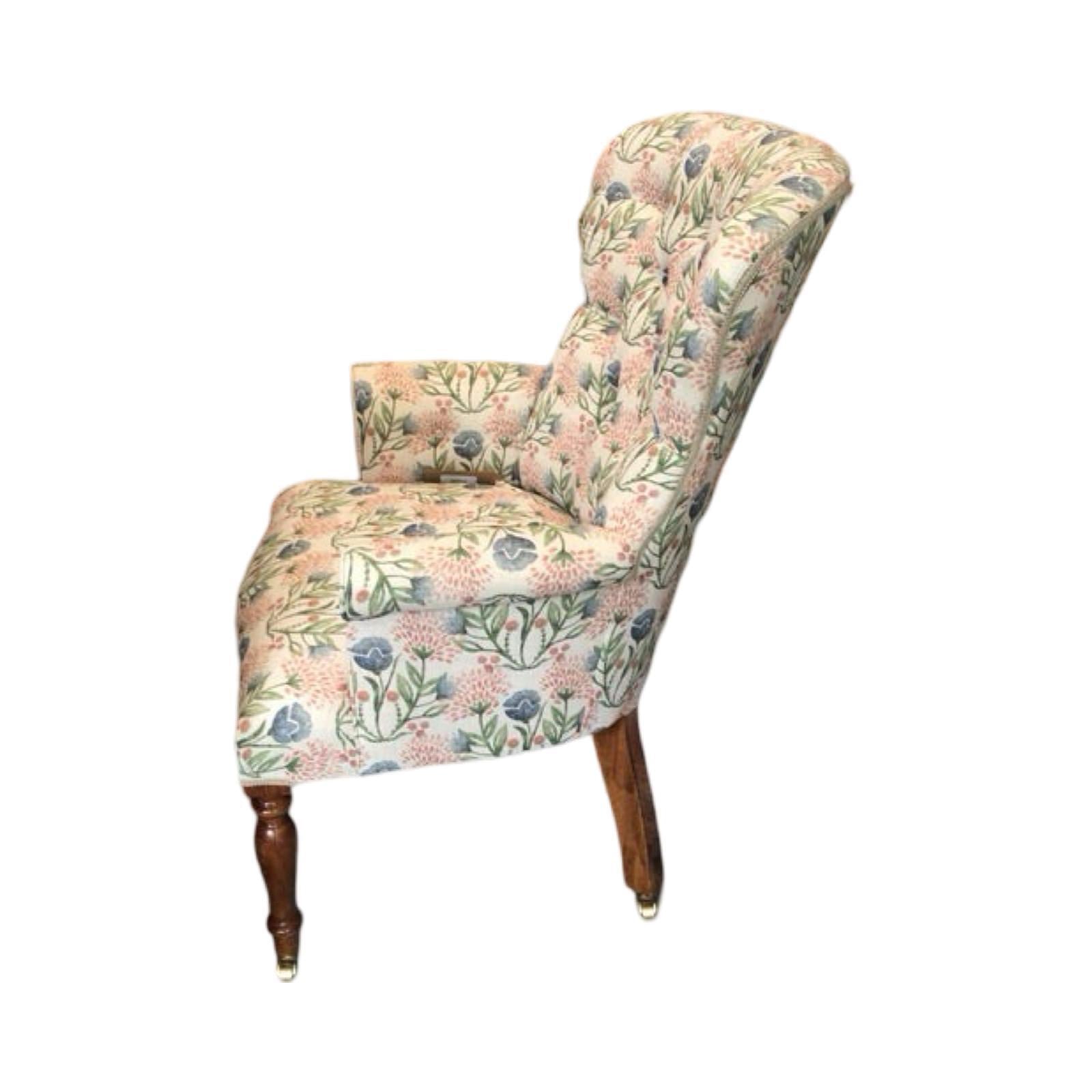 A cream linen armchair with pink and pale blue floral pattern, featuring mahogany legs and gold castors, upholstered with a button-back design.