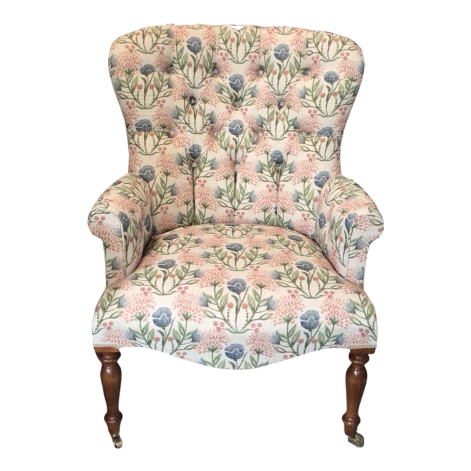 A cream linen armchair with pink and pale blue floral pattern, featuring mahogany legs and gold castors, upholstered with a button-back design.