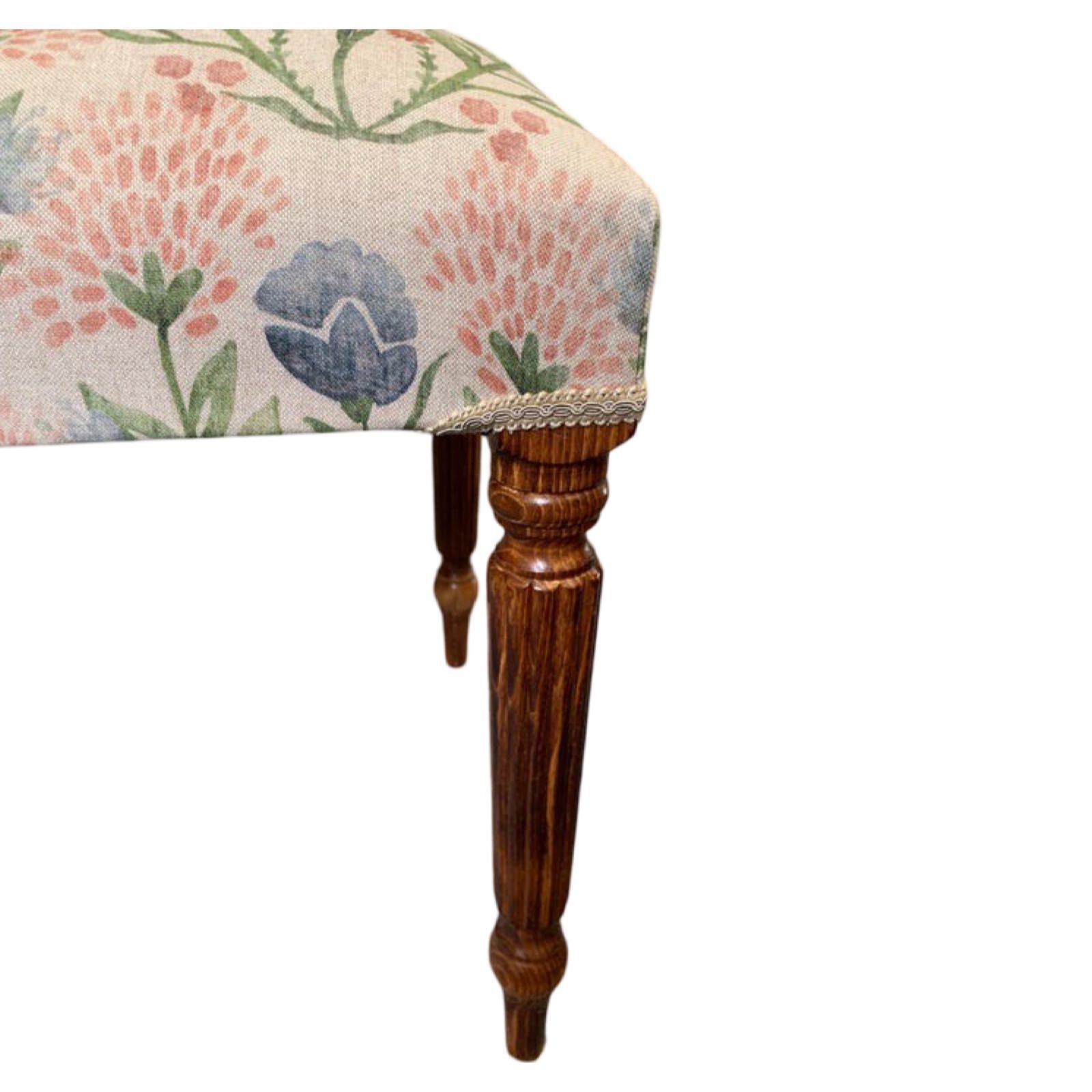 A rectangular bench with mahogany legs and a linen fabric cover featuring a floral pattern in pink, blue, and green.