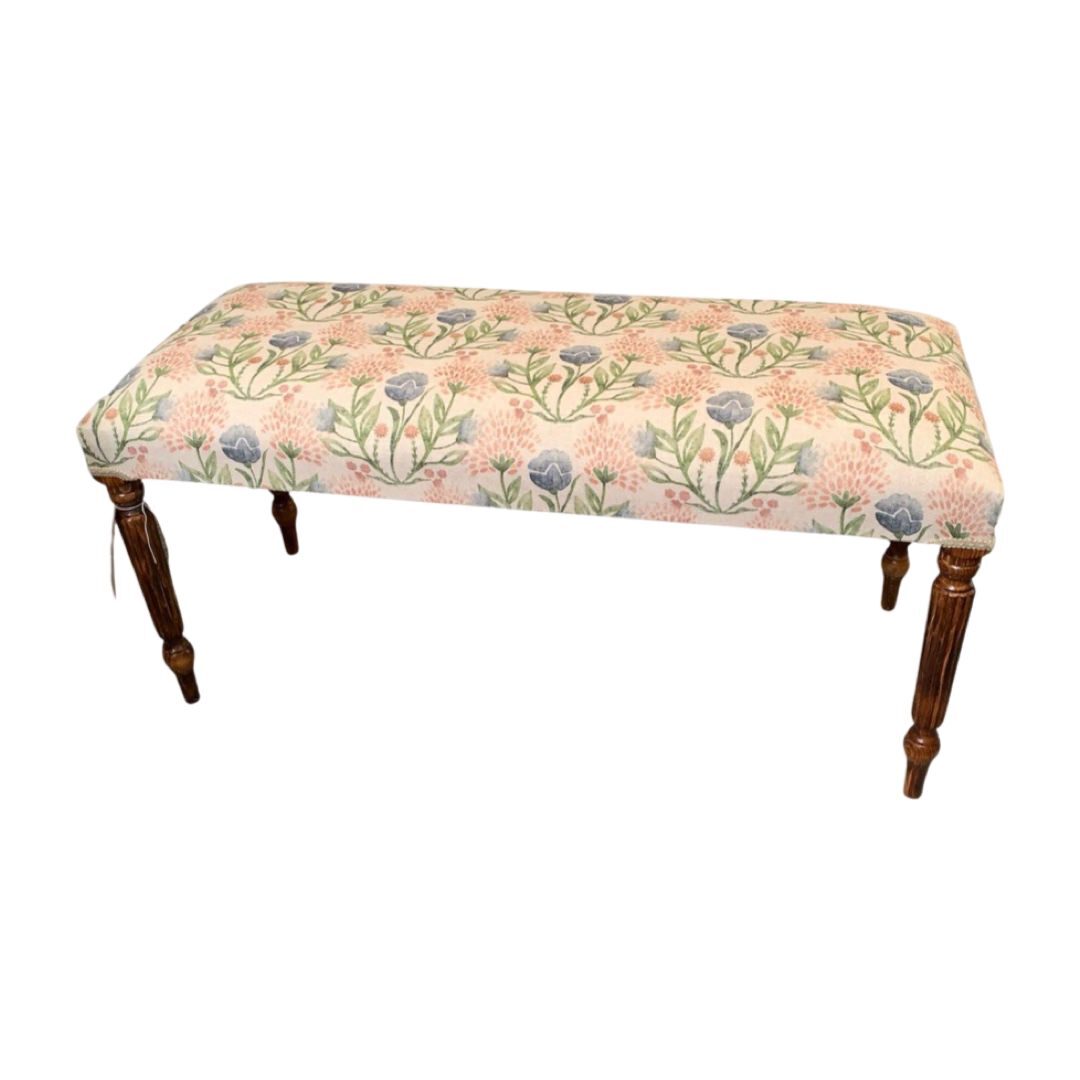 A rectangular bench with mahogany legs and a linen fabric cover featuring a floral pattern in pink, blue, and green.