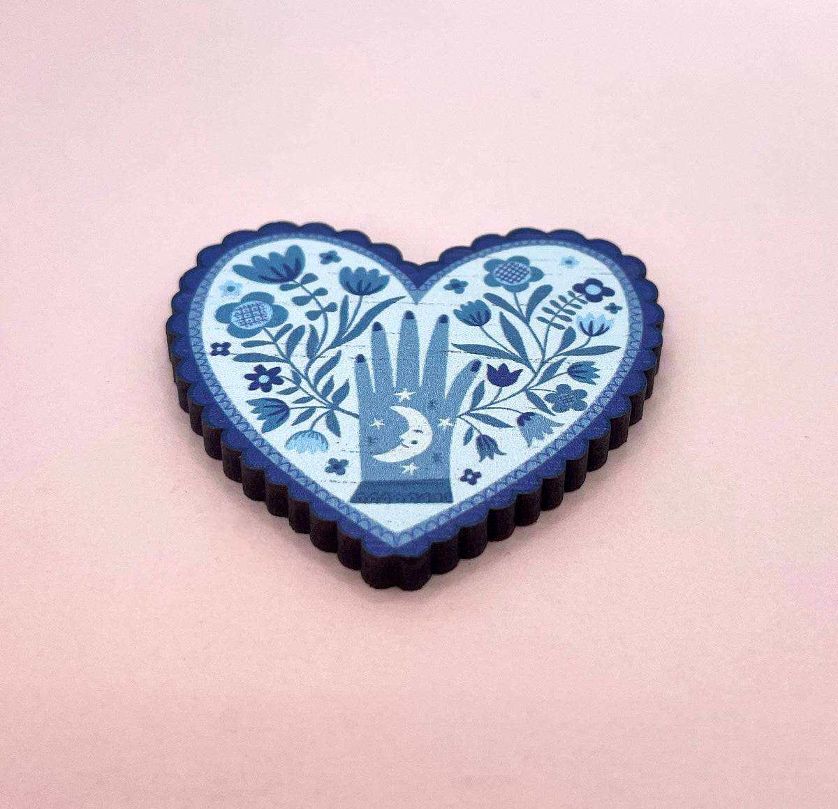 Heart-shaped blue decorative item with floral and hand design on a pink background.