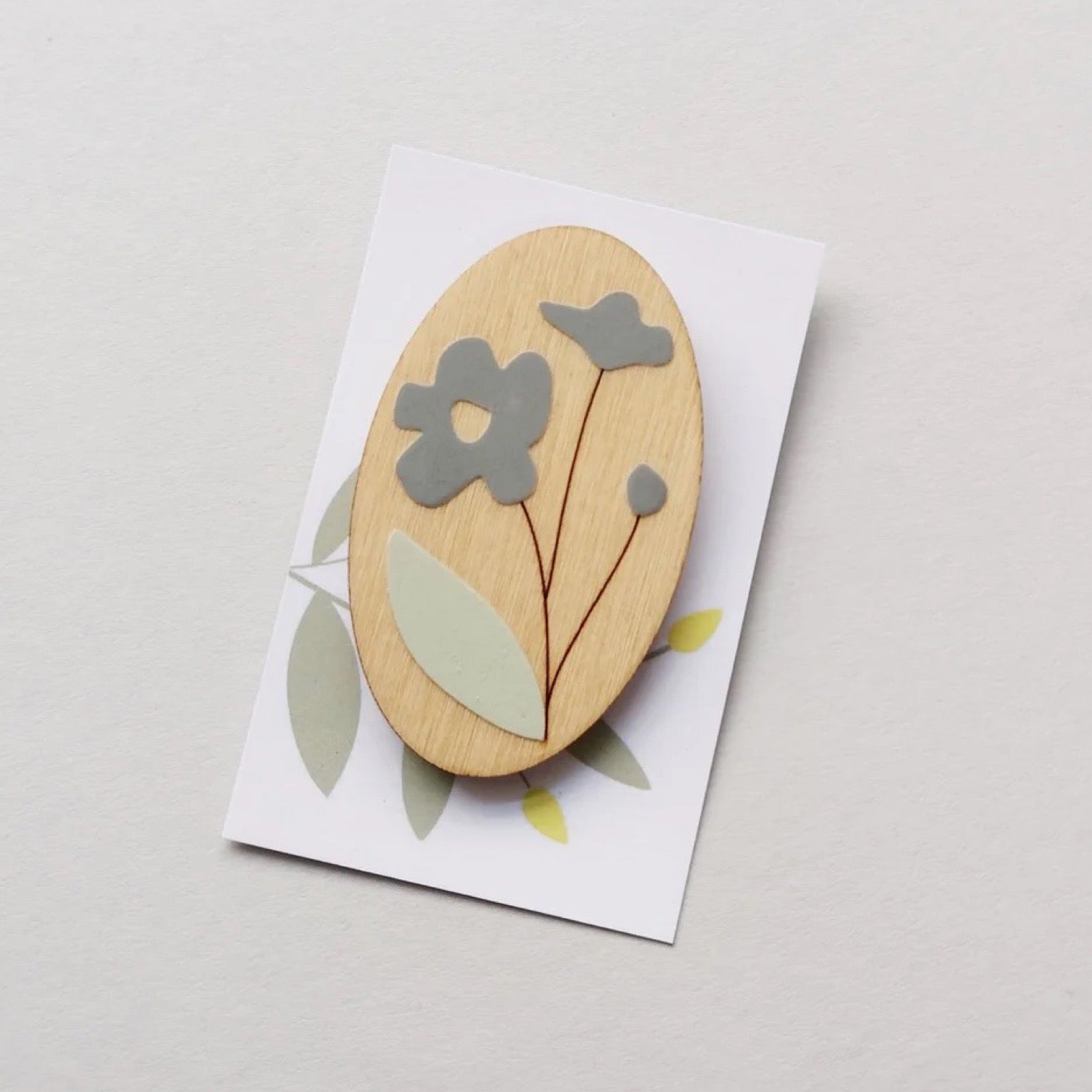 Wooden brooch with floral design on a white card against a light grey background.